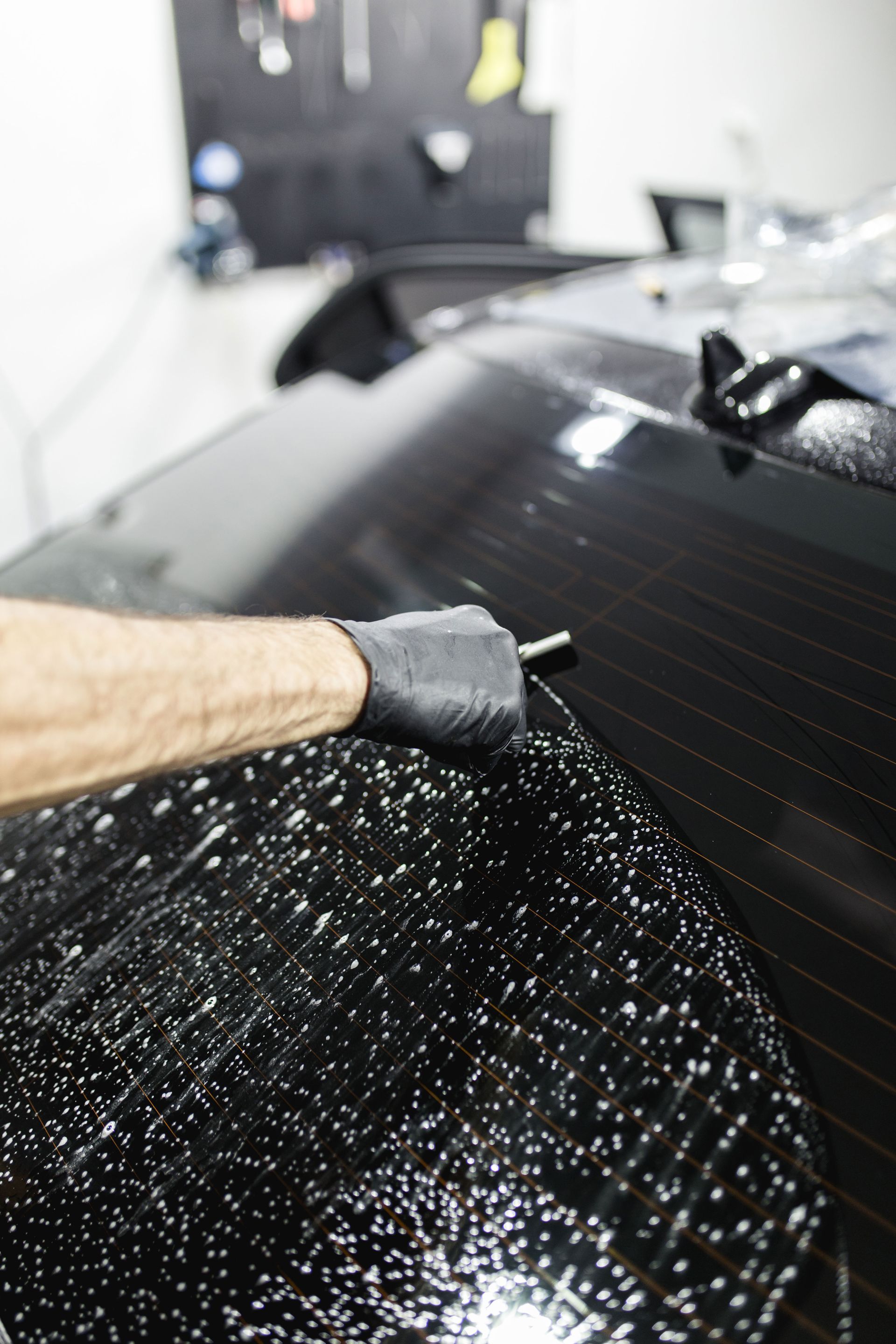 Gloved hand waxing a black car hood with speckled polishing compound
