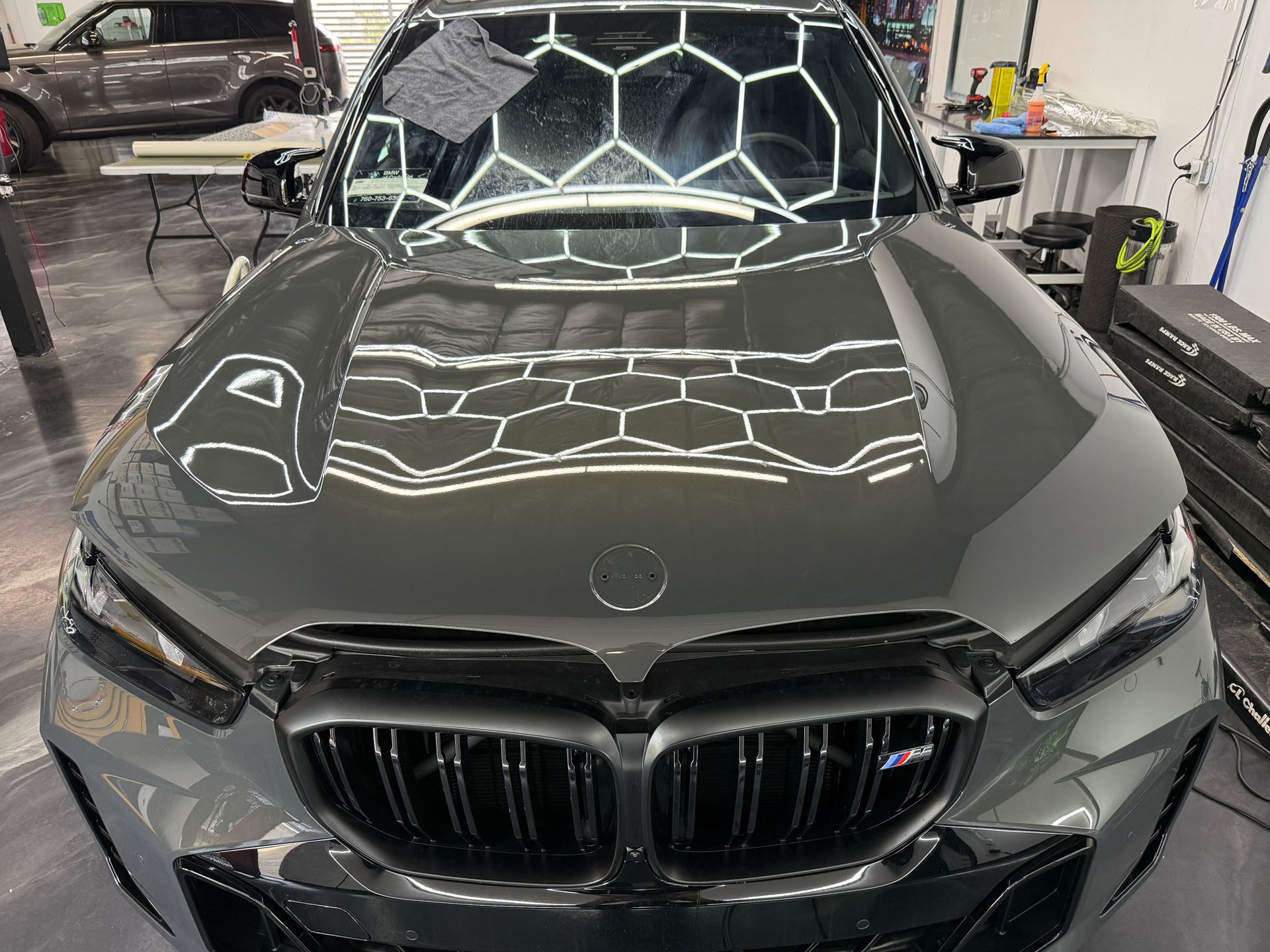 Front view of a black BMW sedan in a garage, with bright ceiling lights reflected on the hood.