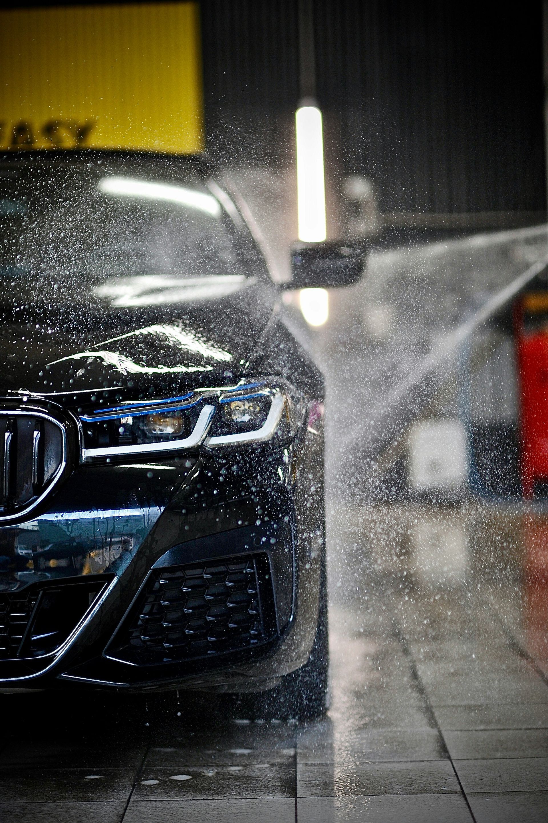 Black BMW being sprayed at a car wash at night, water mist and reflections on wet pavement