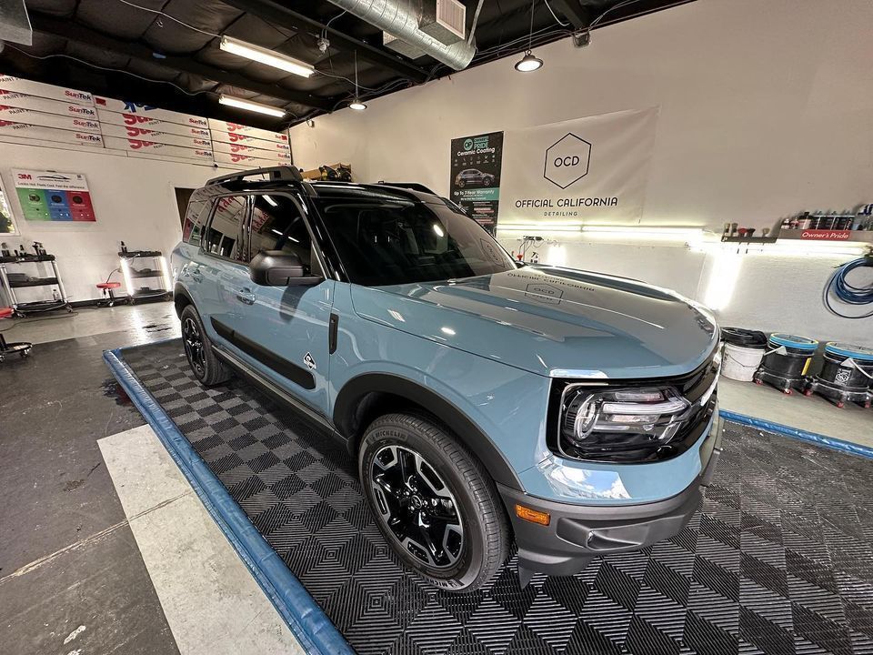 Light blue SUV in an auto shop on a lift, viewed from the front-left side.