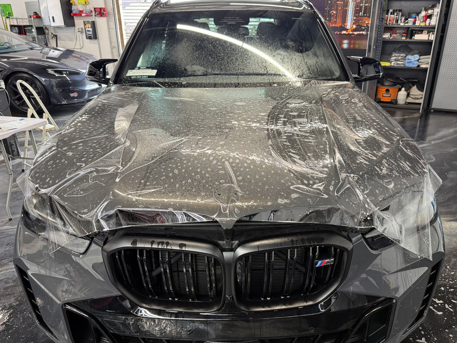 Black BMW sedan covered in shattered glass and debris inside an auto shop garage
