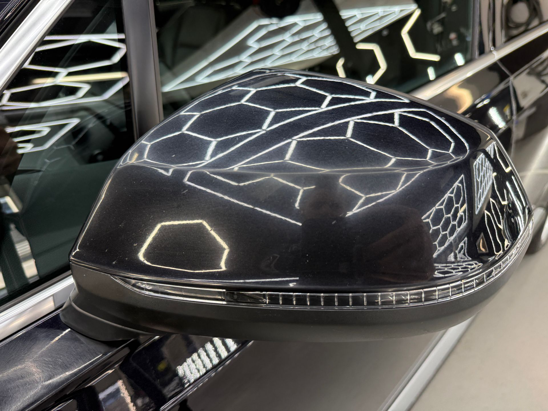 Black car side mirror reflecting bright geometric lights in a dark showroom