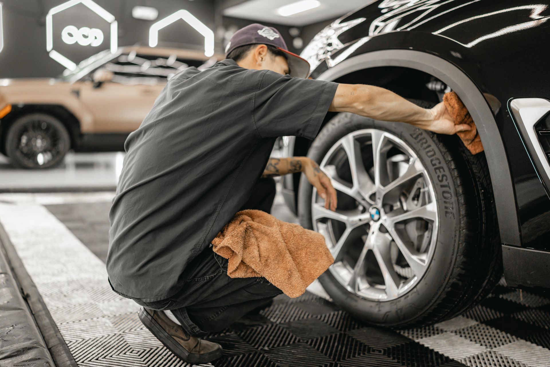 Mechanic wiping the front wheel of a black car in a garage detail bay