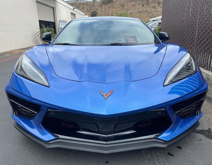 Blue sports car seen from the front in a driveway, with sharp headlights and black accents.
