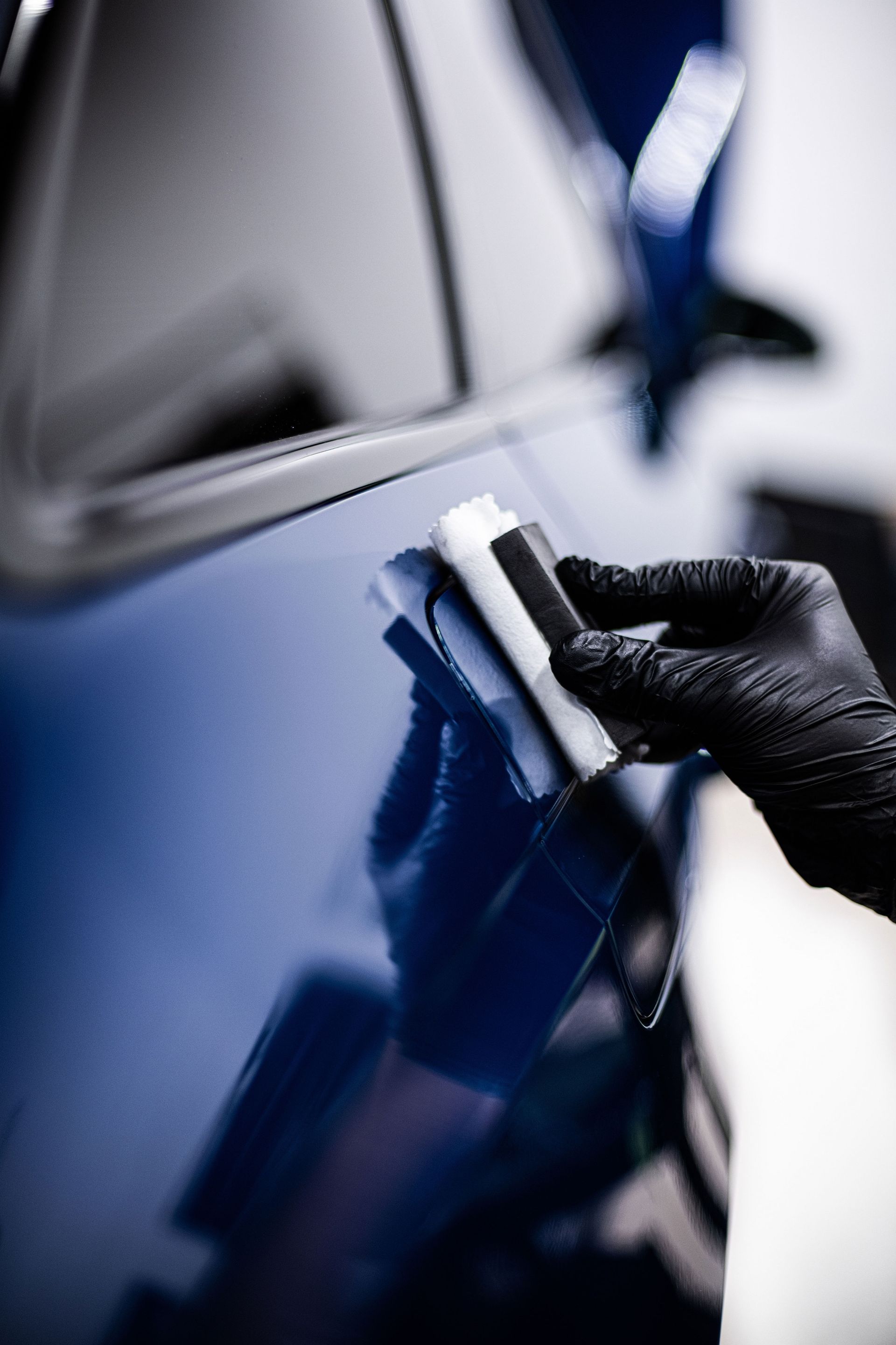 Gloved hand polishing a blue car door with a cloth, close-up
