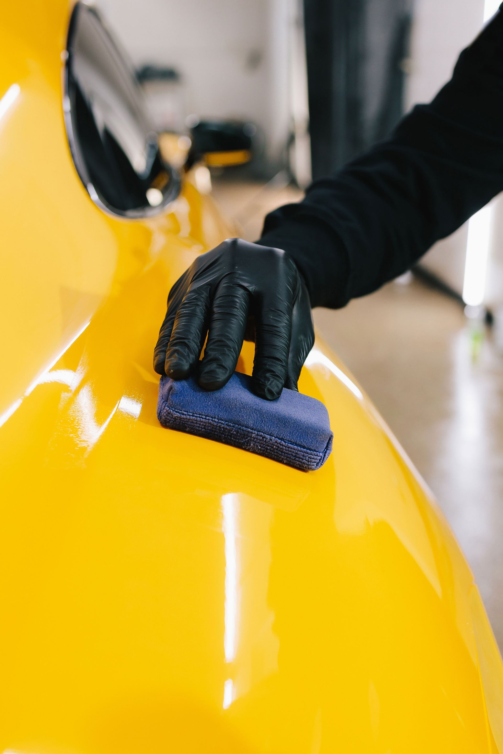 Gloved hand polishing a yellow car with a blue cloth
