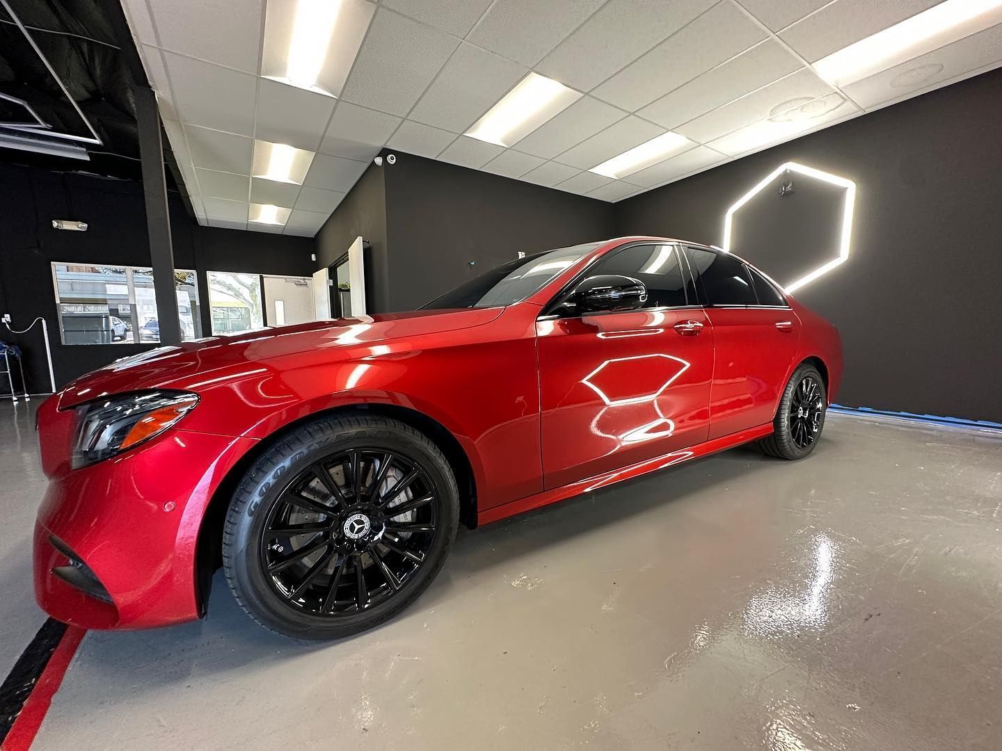 Red sports sedan in a showroom with black wheels and gray walls