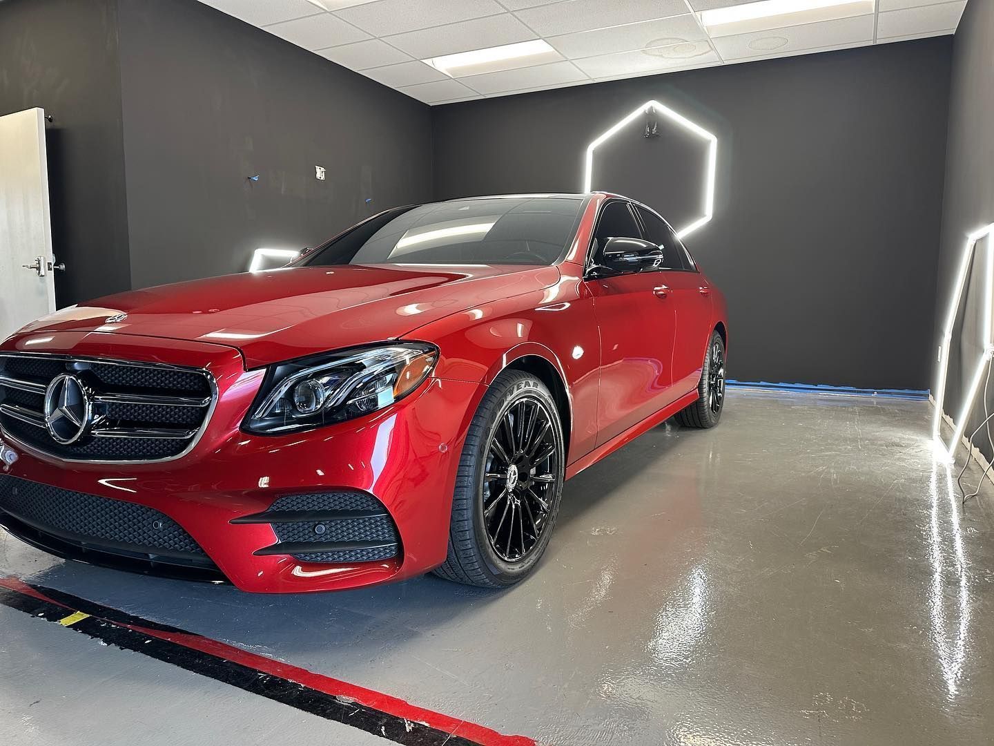 Red Mercedes-Benz sedan in a glossy showroom with dark walls and neon-lit hexagon accents