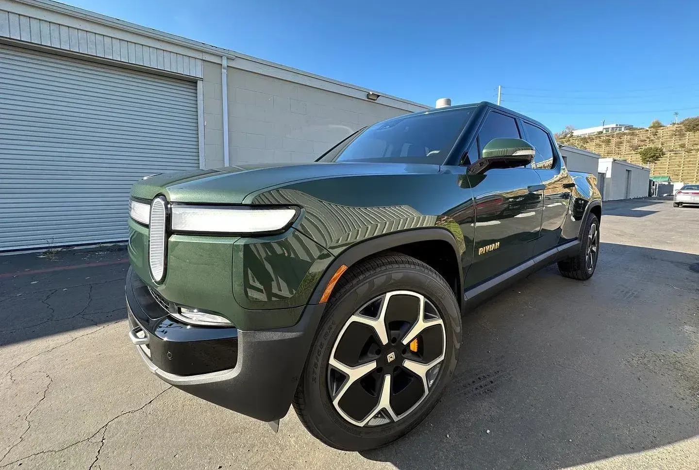 Dark green pickup truck parked beside a white industrial building on a sunny street.