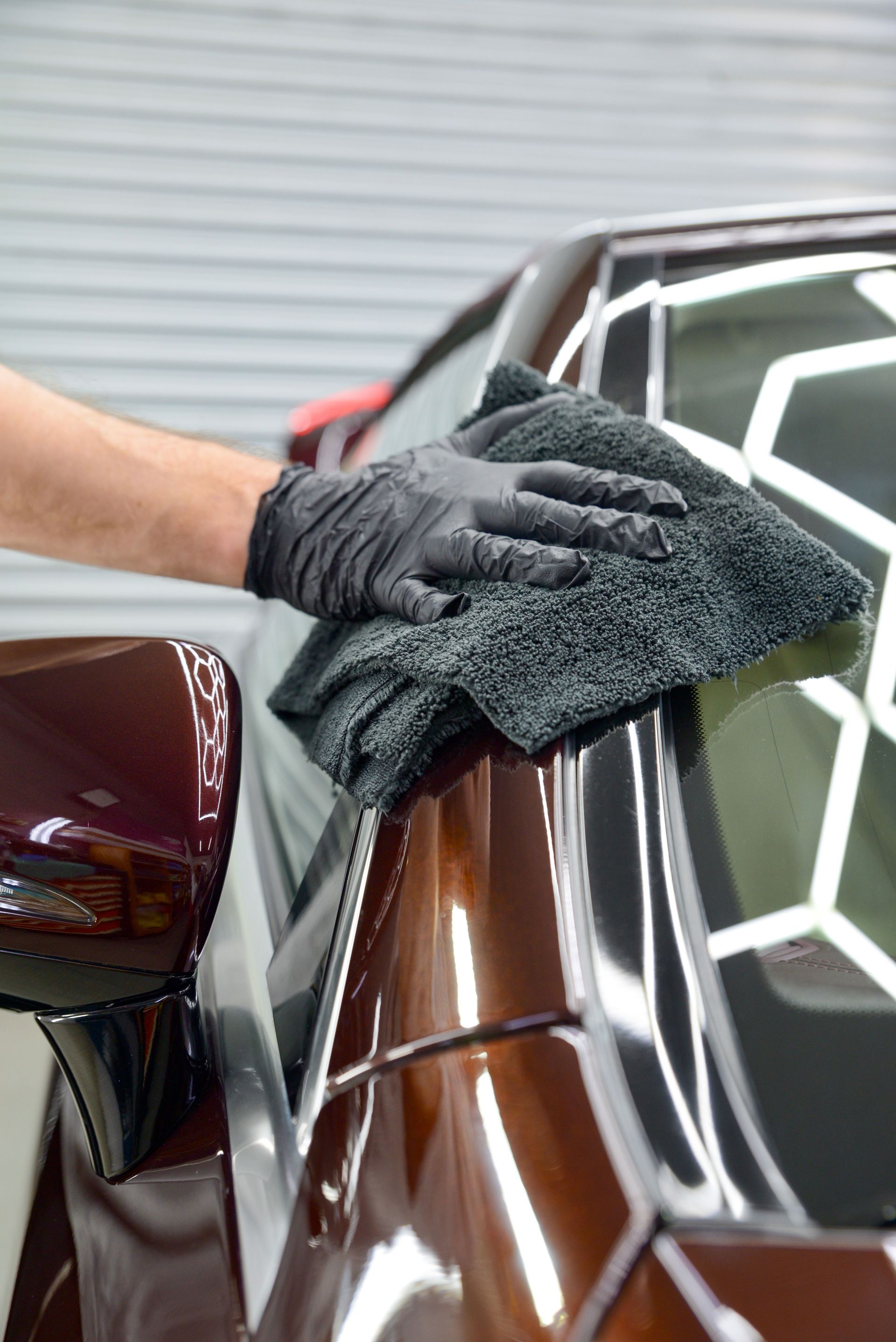 Gloved hand polishing a brown car’s fender with a microfiber cloth in a garage
