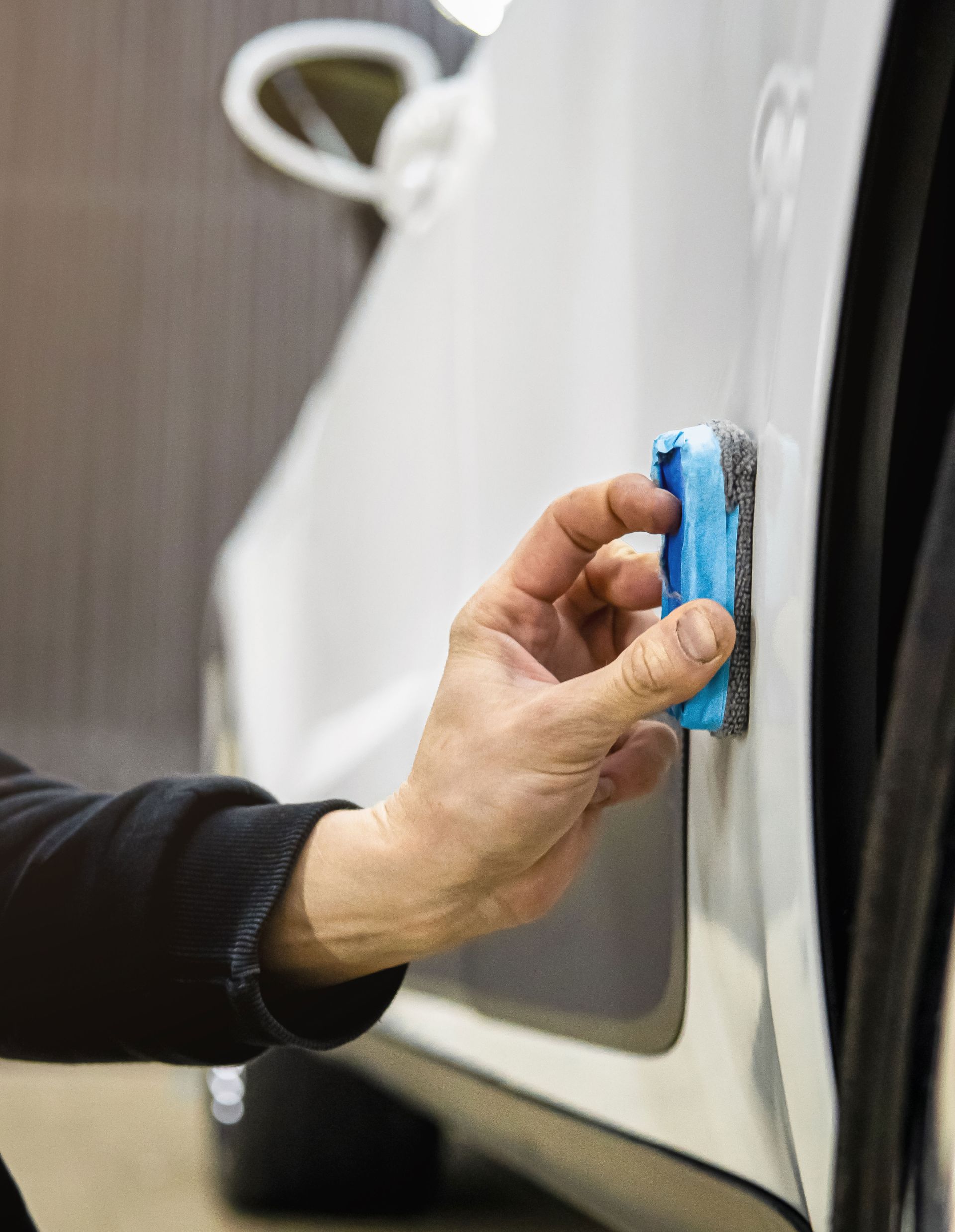 Hand wiping a white car with a blue sponge near the side panel
