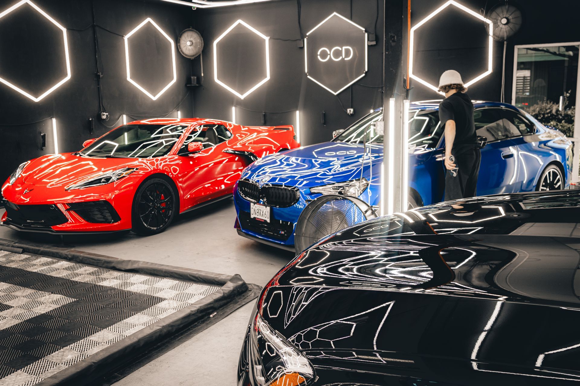 Red, blue, and black sports cars on display in a showroom with geometric wall lights.