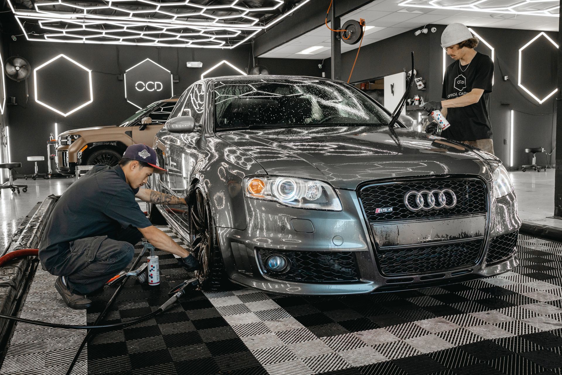 Two workers detailing a black Audi inside a modern car wash or auto detailing shop