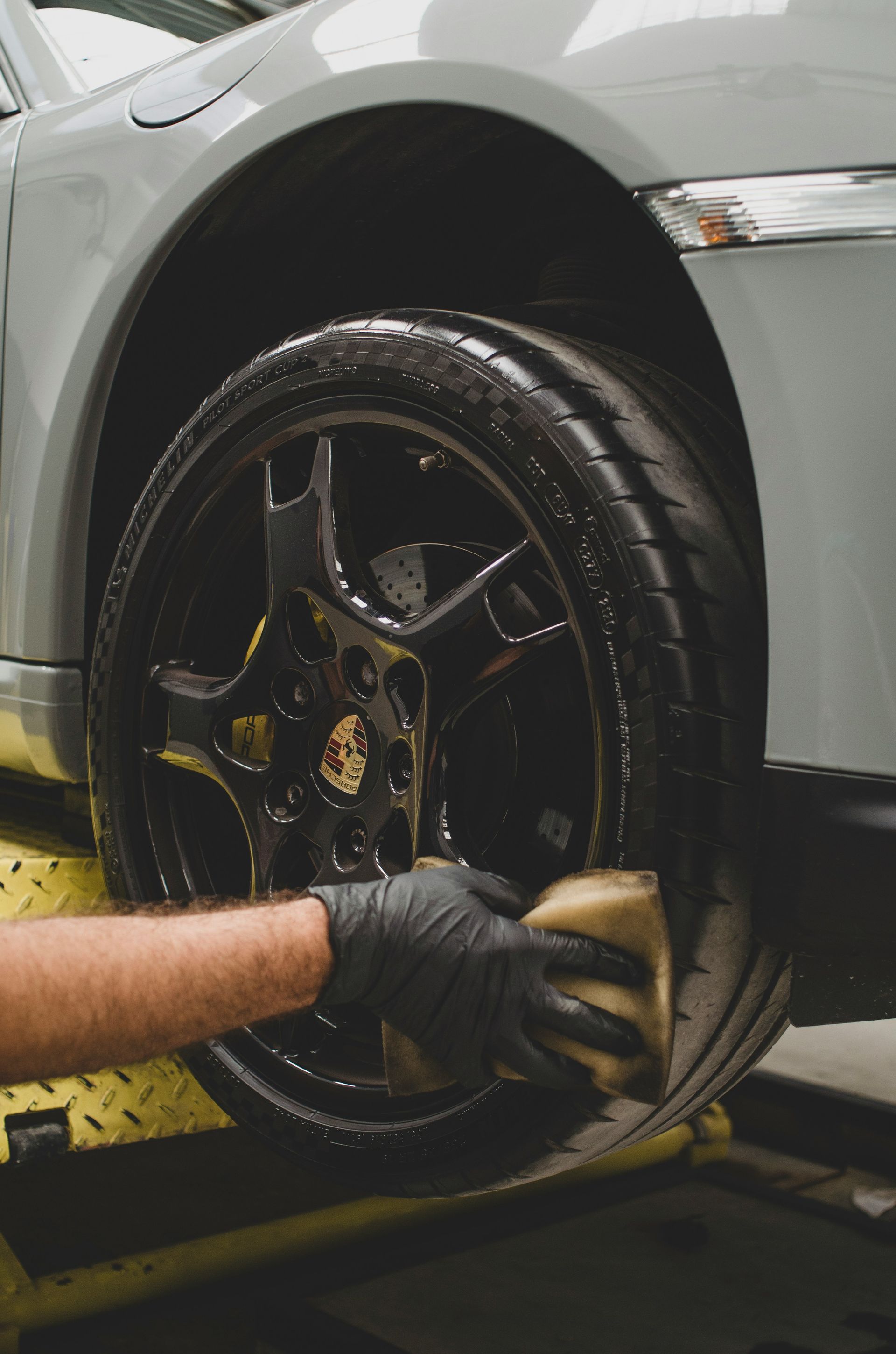 Gloved hand polishing a black car tire on a silver vehicle in a garage