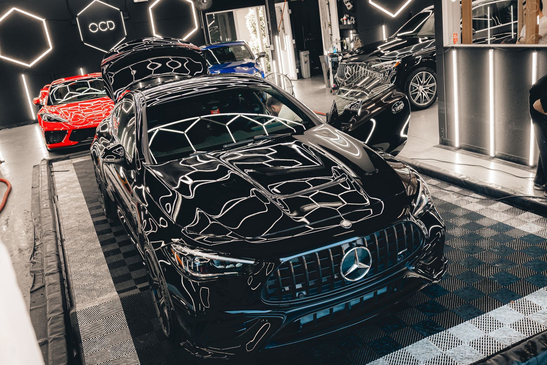 Black Mercedes sports car displayed in a glossy showroom with neon reflections and other cars in the background