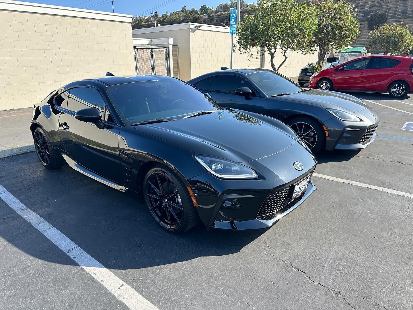 Black sports coupe parked in a lot, with a silver car and red SUV behind it.