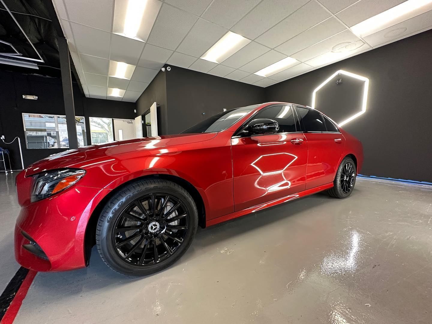Red sports sedan in a showroom with black wheels and neon wall light