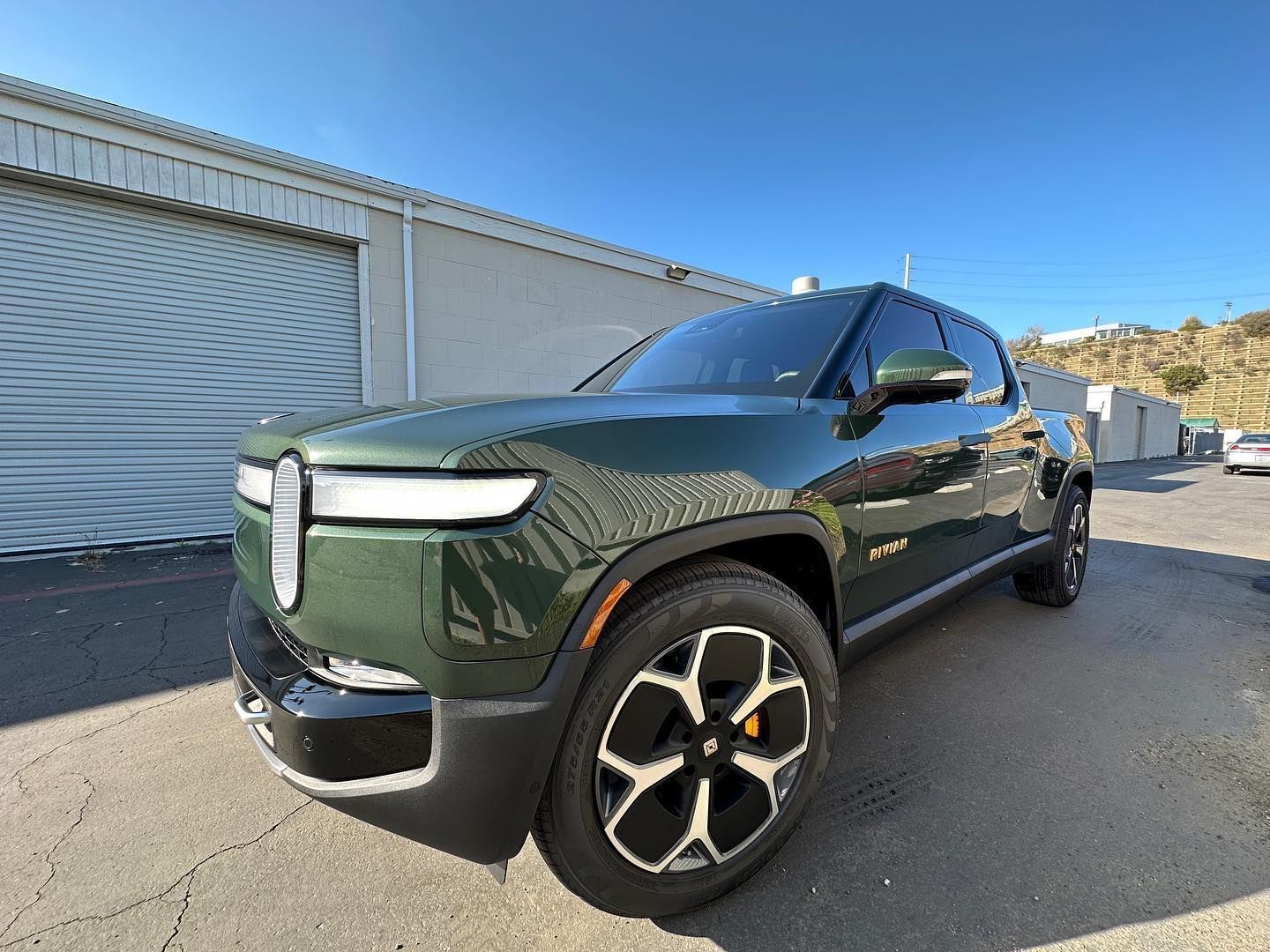 Dark green SUV parked outdoors beside industrial buildings under a clear blue sky