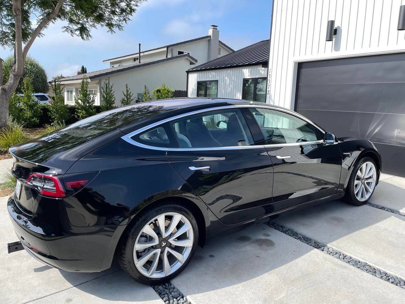 Black Tesla sedan parked in a driveway beside a garage and modern house