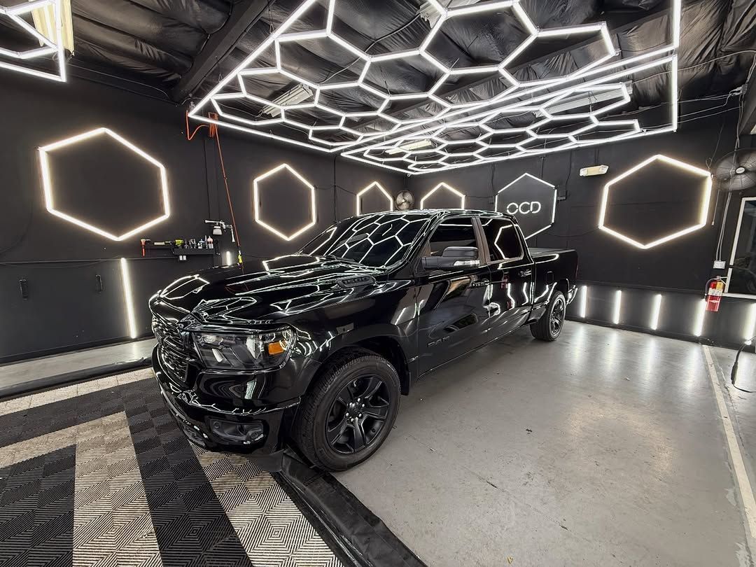 Black pickup truck in a neon-lit showroom with geometric ceiling lights and glossy black walls