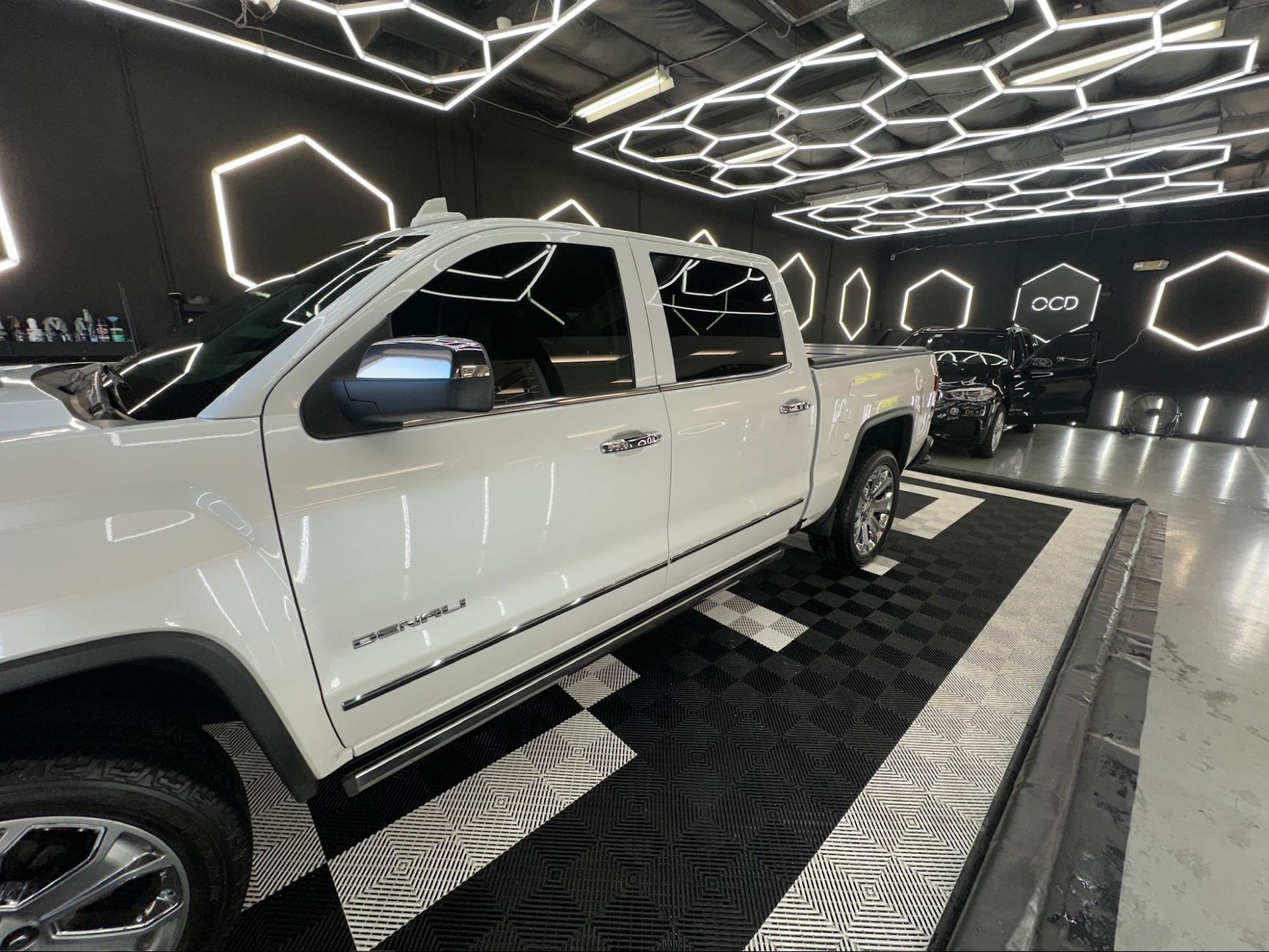 White pickup truck on a patterned floor in a futuristic showroom with glowing hexagonal lights.