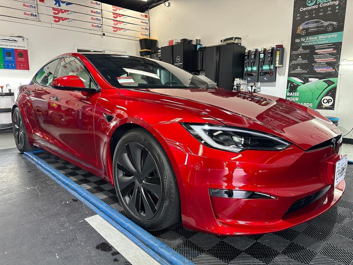 Red Tesla sedan in a garage, shown on a lift with black wheels and glossy red paint