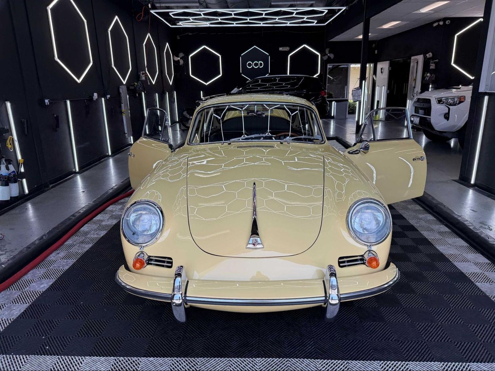 Vintage beige car displayed indoors under geometric lights in a modern showroom