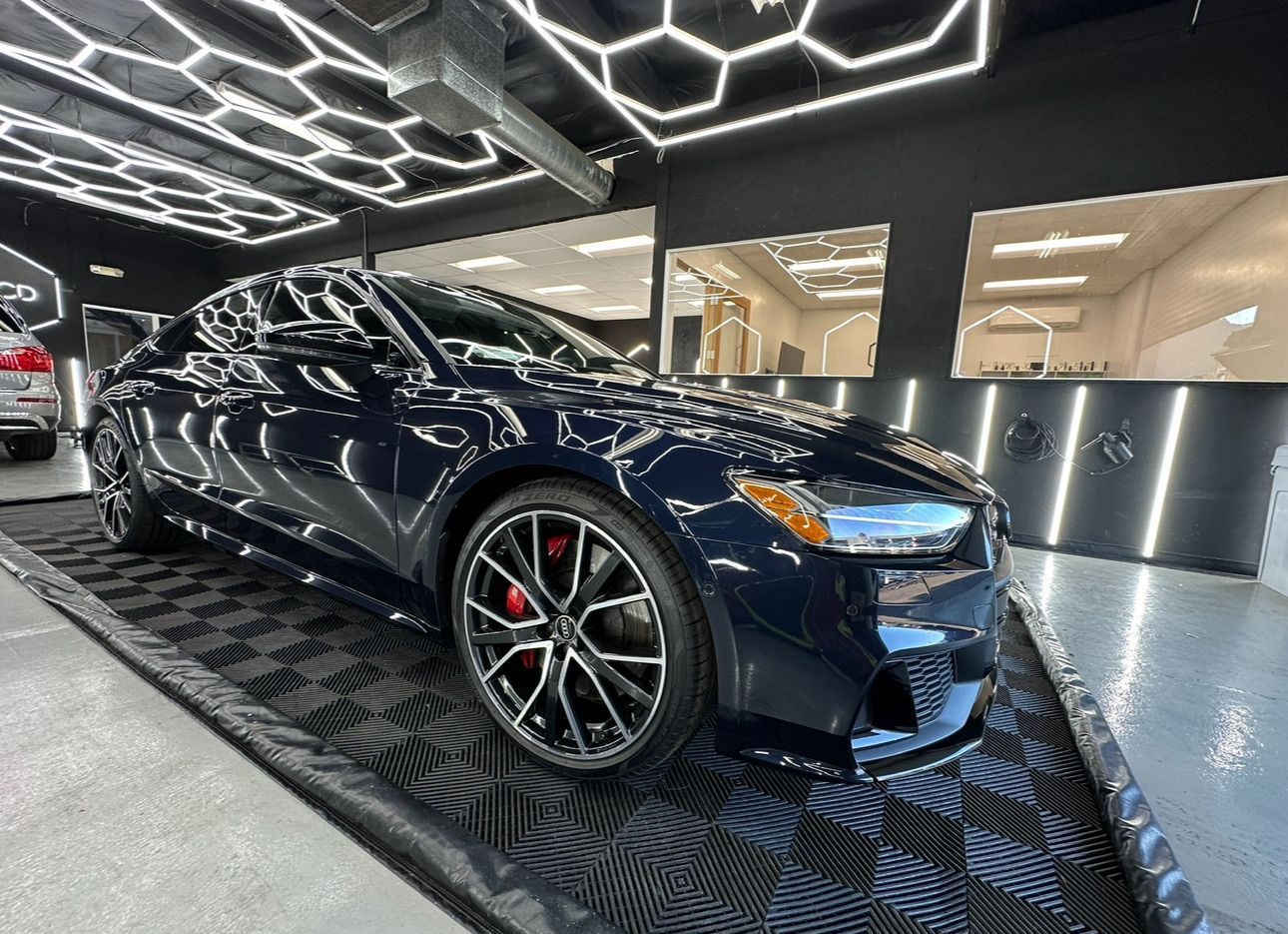 Dark blue luxury sedan in a showroom with hexagonal ceiling lights and patterned floor