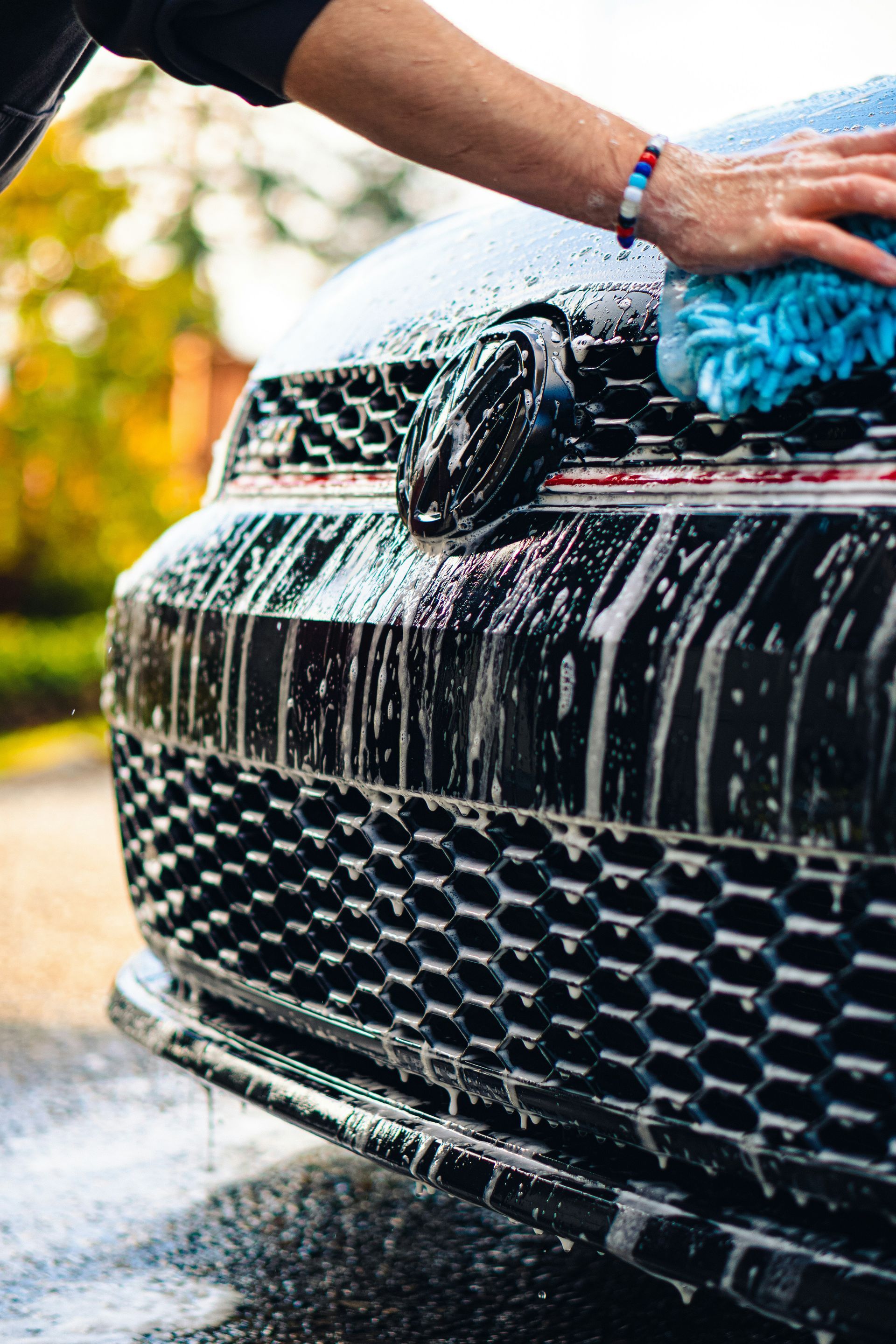 Person washing a black car with soap and water in a driveway