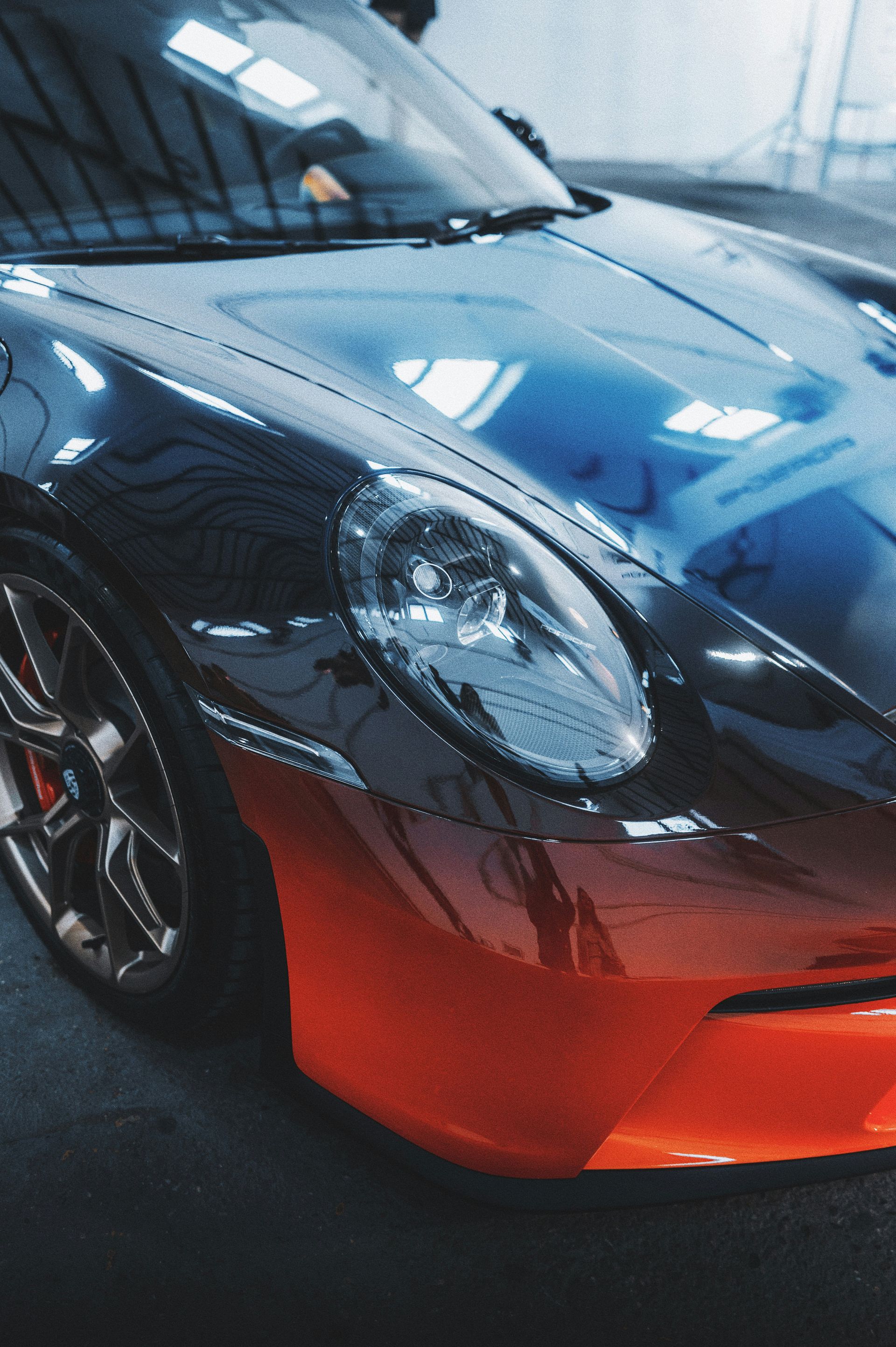 Close-up of a blue and red sports car in a showroom, showing the front headlight and hood
