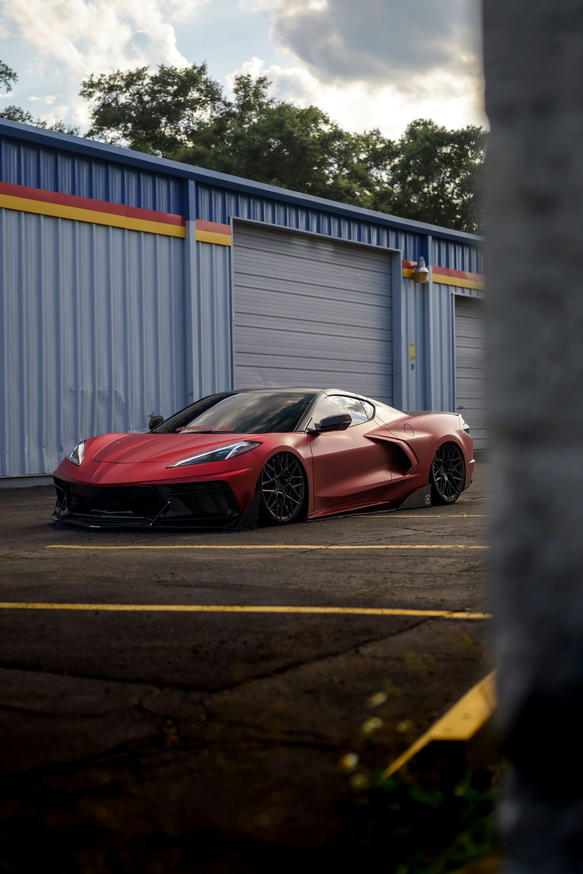 Red sports car parked by a blue warehouse at dusk