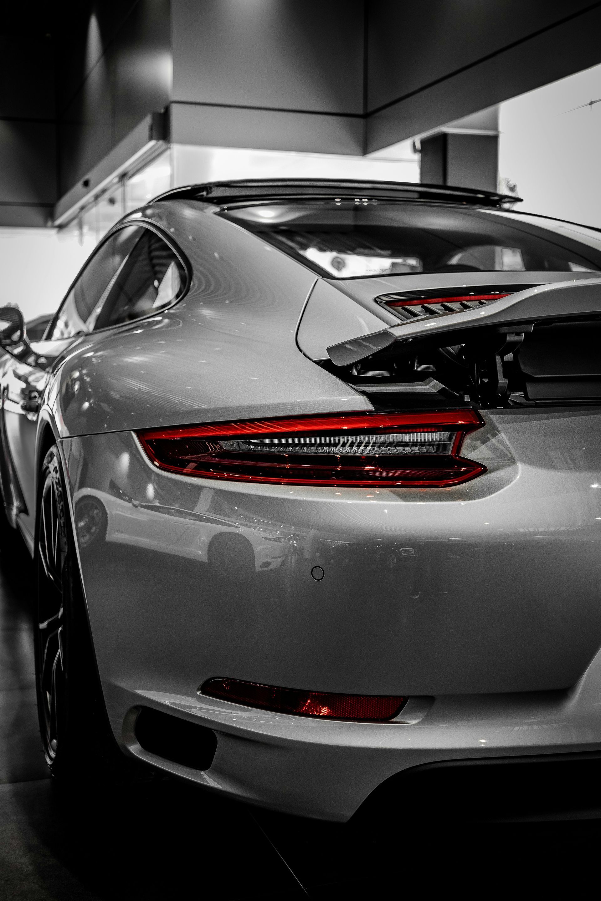 Silver sports car parked indoors, rear view with sleek taillights in a showroom-like setting