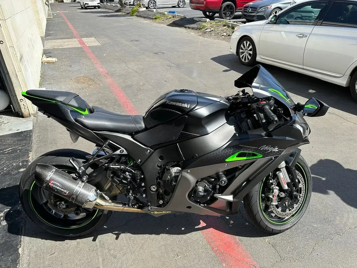 Black sport motorcycle with green accents parked on a street beside a silver car