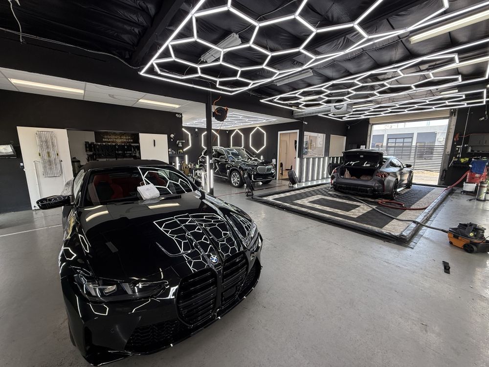 Black car in a modern auto detailing garage with hexagonal ceiling lights and another car in the background