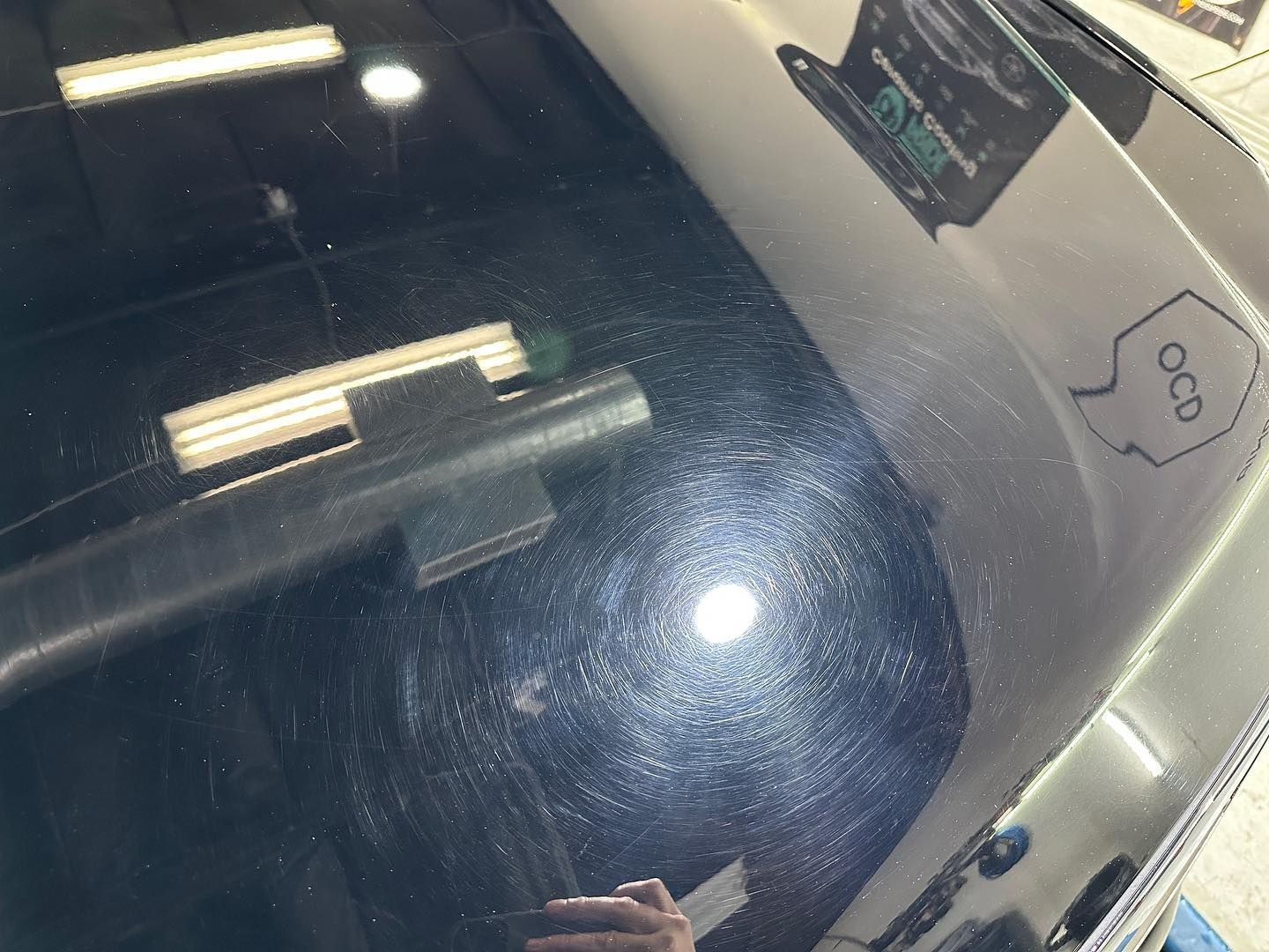 Close-up of a dirty car windshield reflecting fluorescent lights and a nearby parking sign.