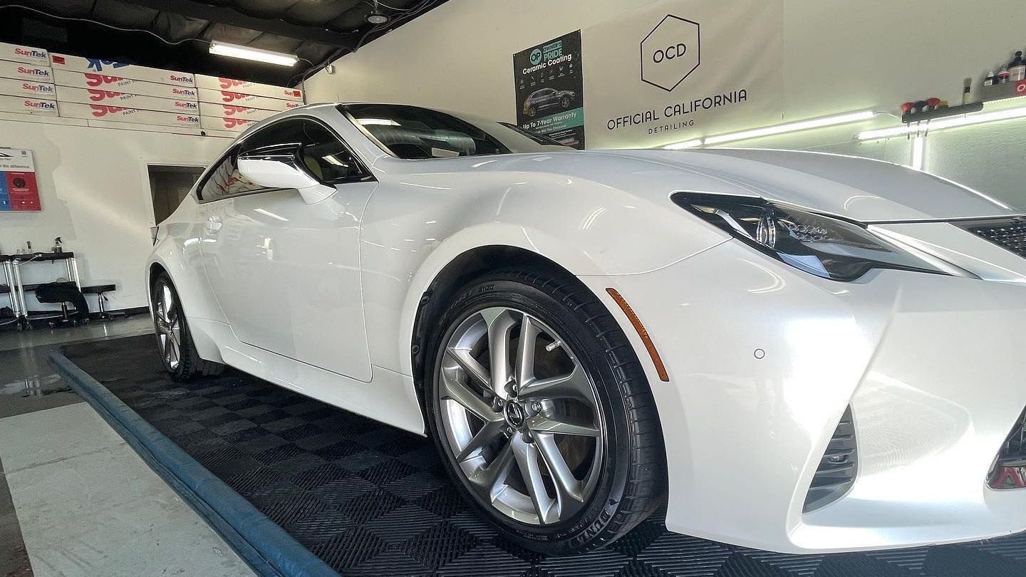 White sports coupe displayed indoors in a showroom, angled front view on a platform.
