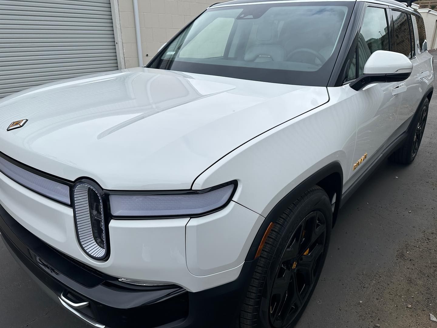 White Rivian SUV parked outdoors, front-left view with black wheels and a chrome grille.