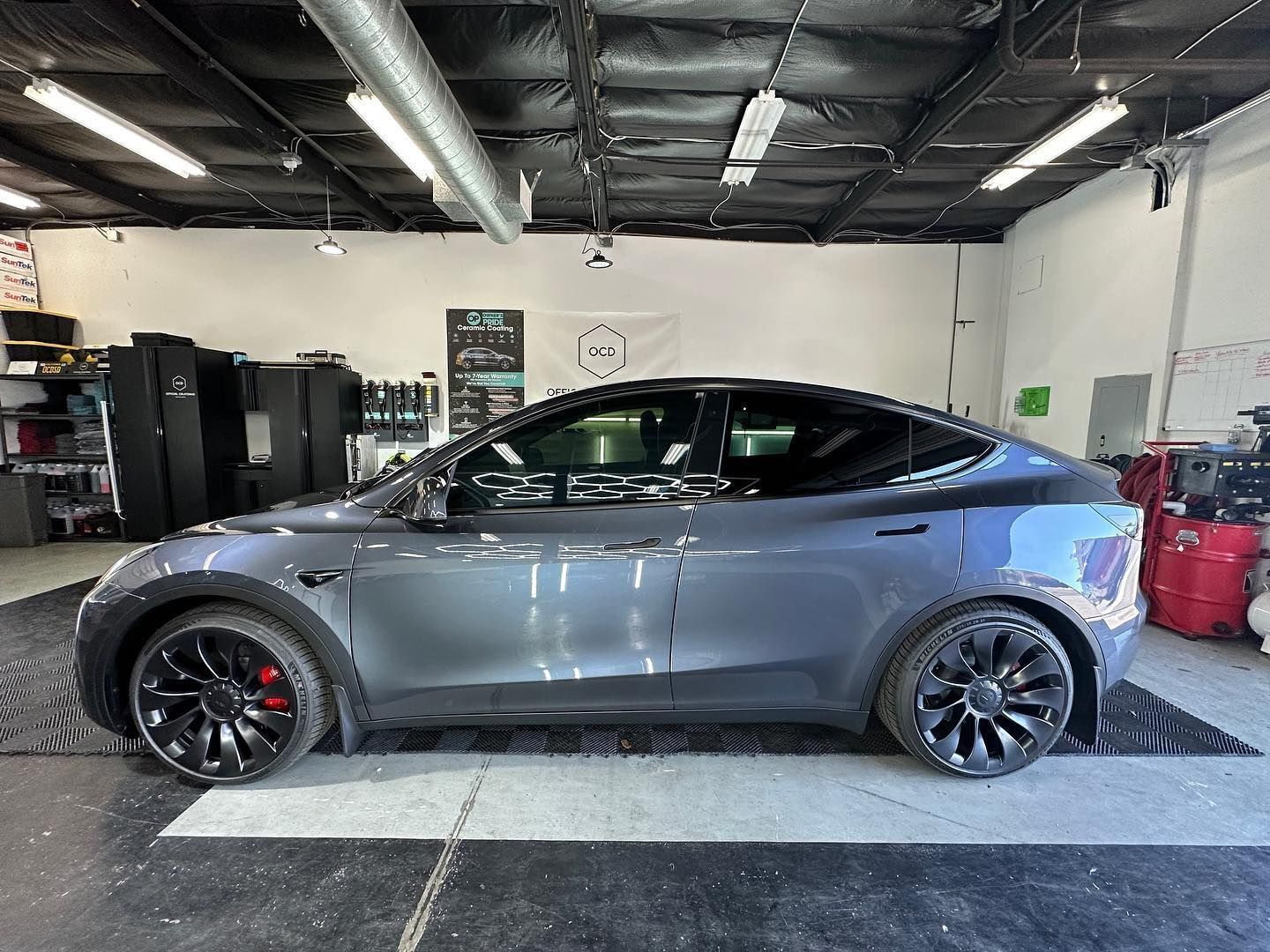 Gray sports car in an auto shop garage, shown in side profile on a lift bay floor.