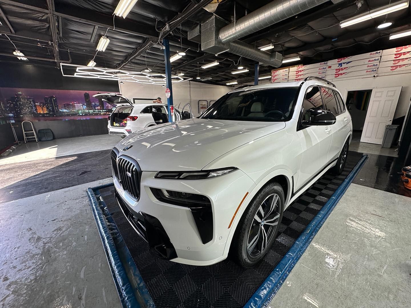 White SUV in a car showroom on a display platform, under bright ceiling lights.