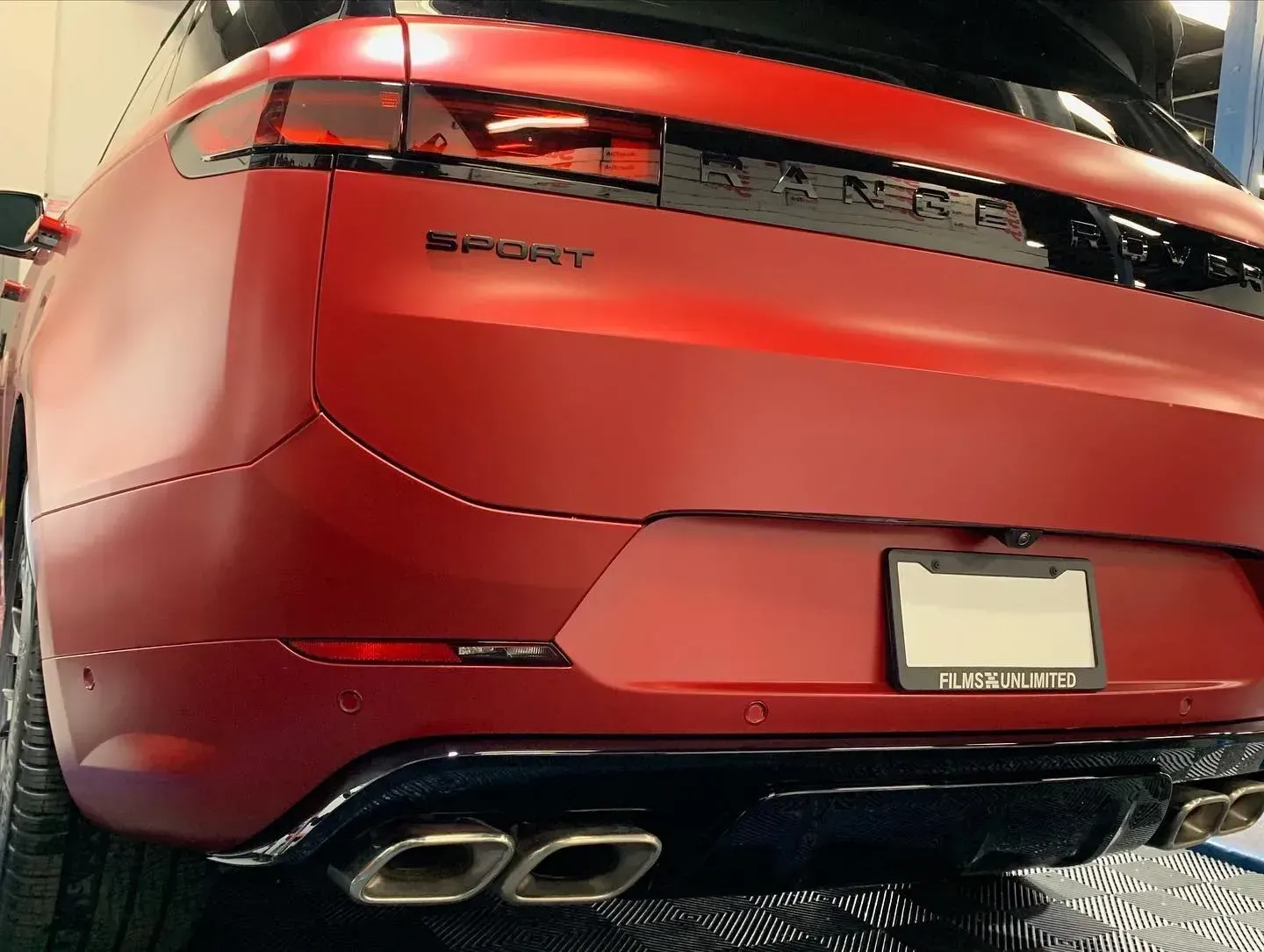 Rear view of a red SUV with quad exhaust pipes and a blurred license plate indoors