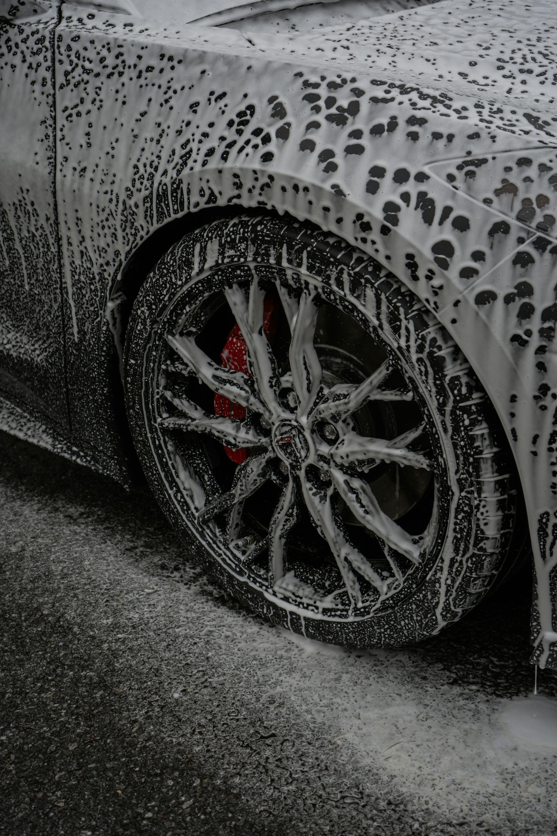 Car covered in soap suds during a car wash, focusing on a wet alloy wheel and tire.