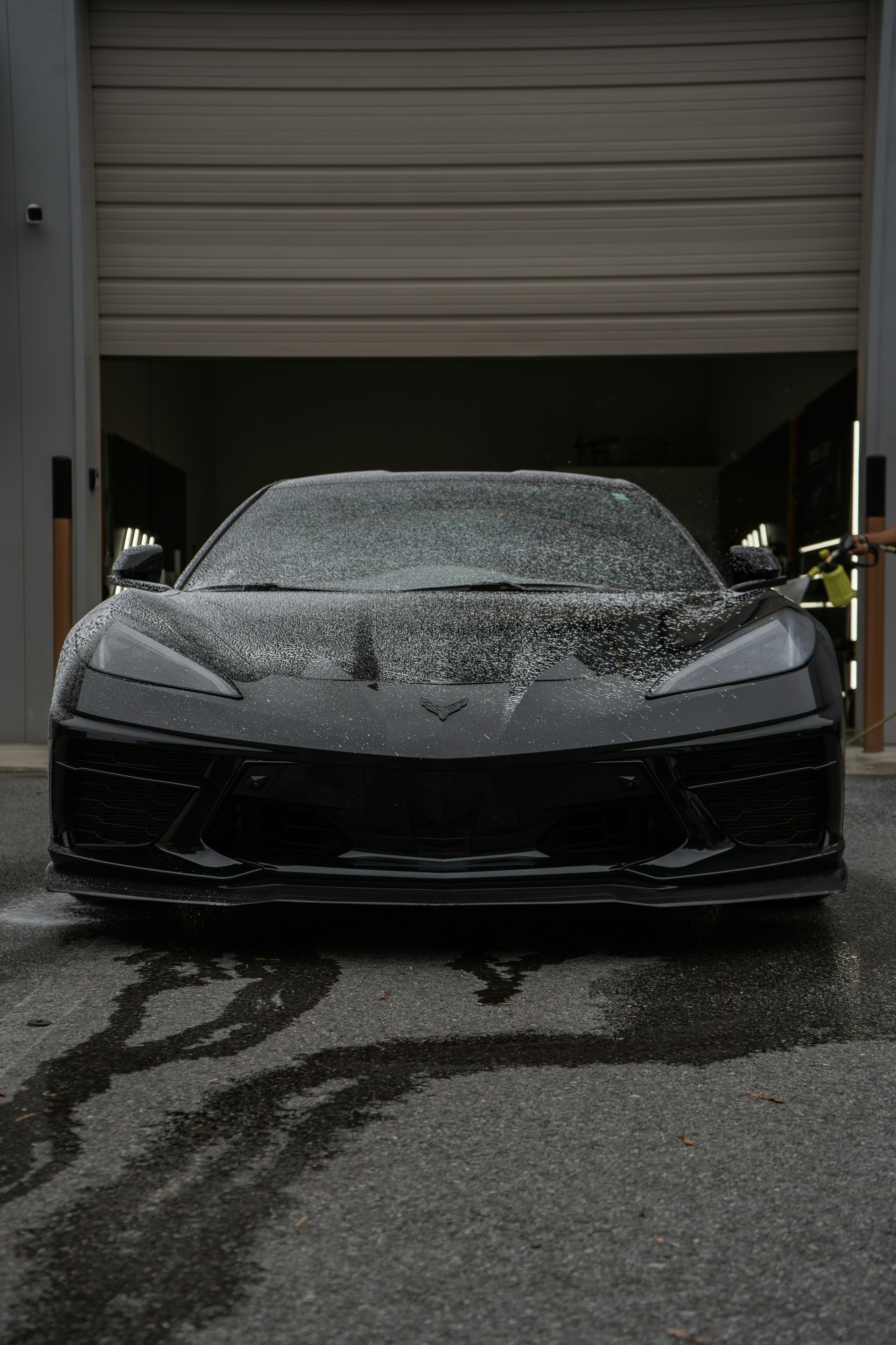 Black sports car covered in soap foam parked in a garage doorway