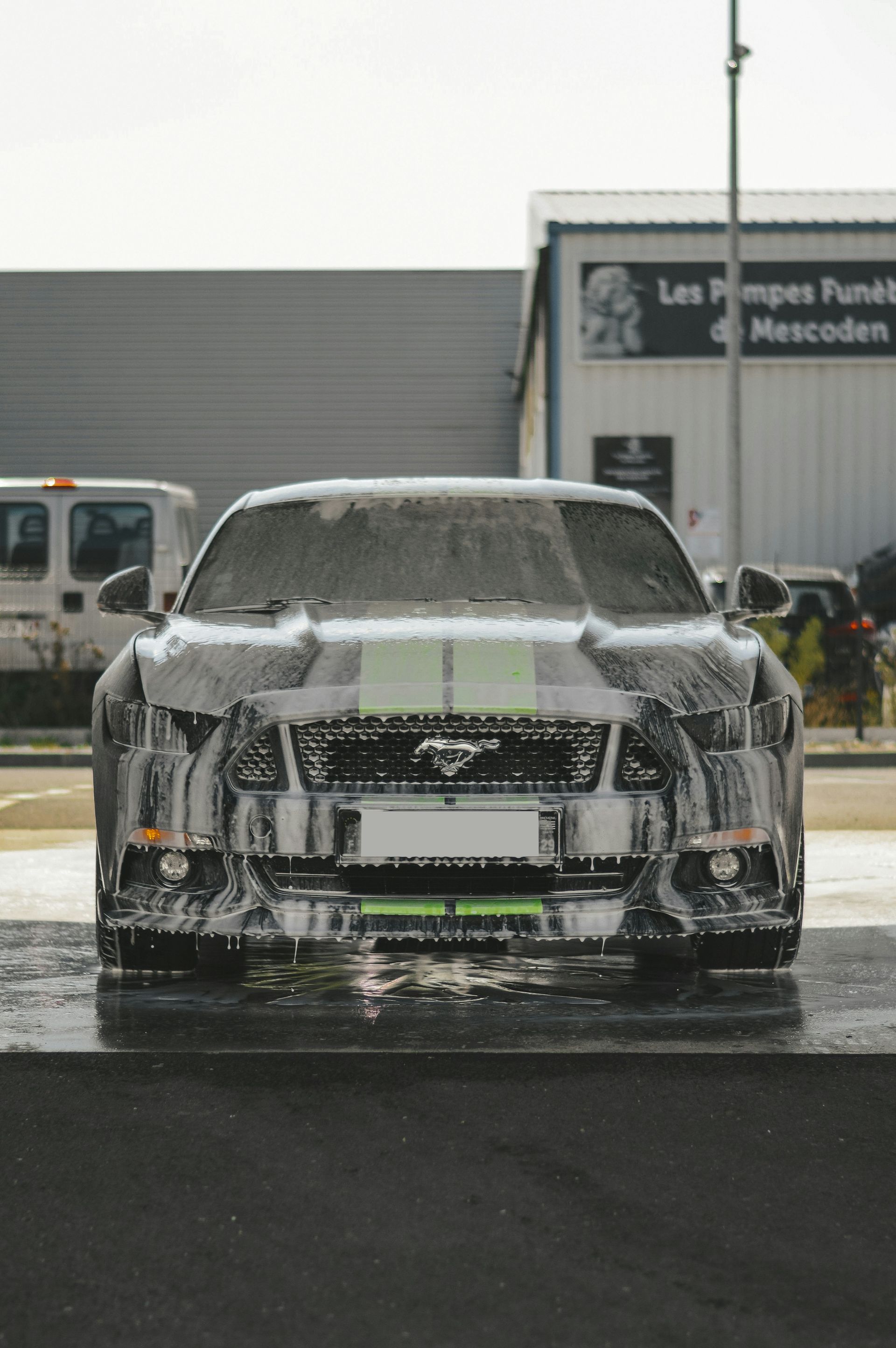 Front view of a silver car covered in white foam at a car wash.