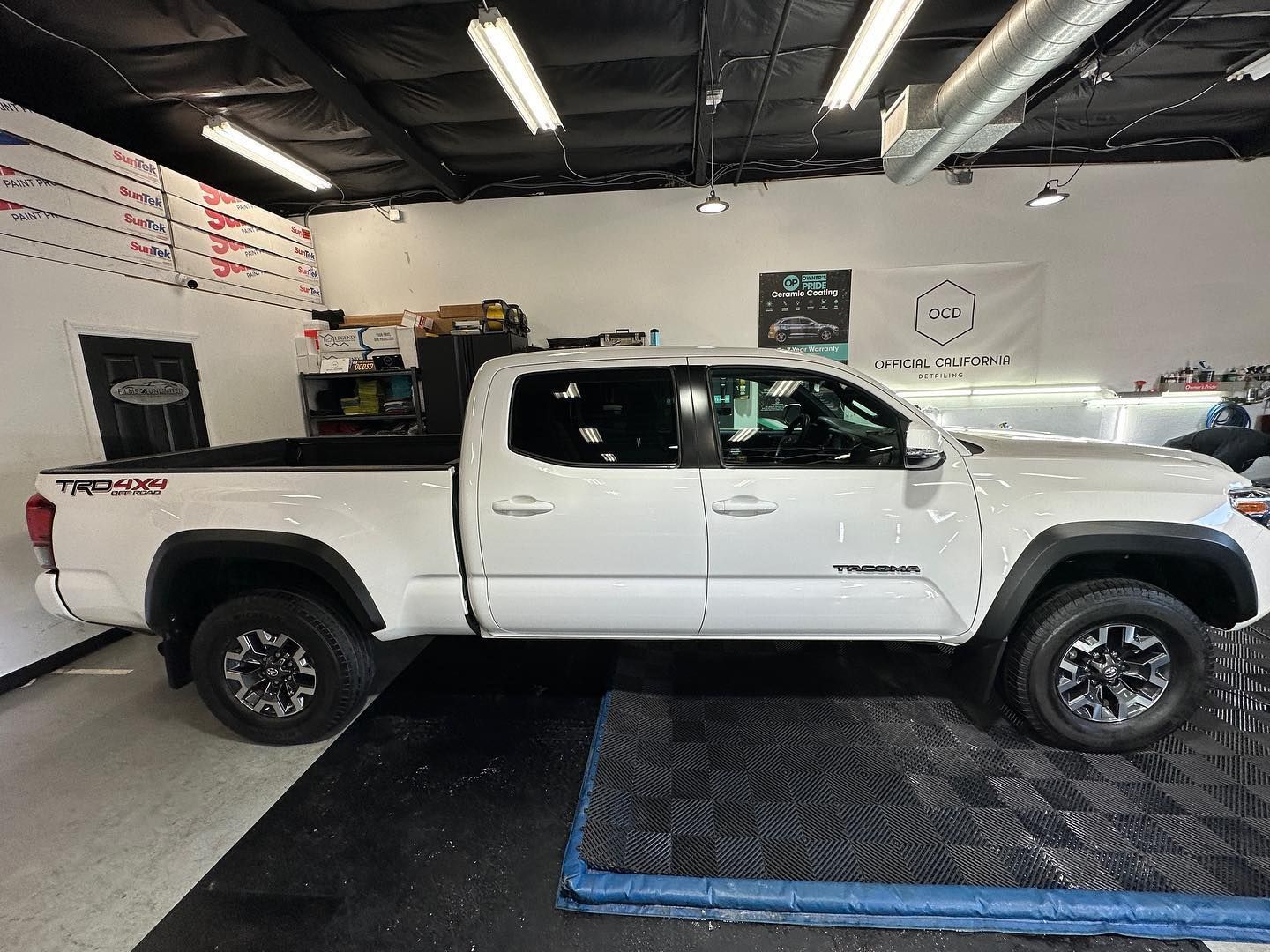 White pickup truck parked inside an auto shop with black wheels and a blue ramp in front