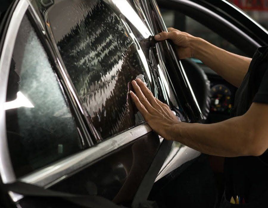 Hands pressing a dark car window film during tint installation