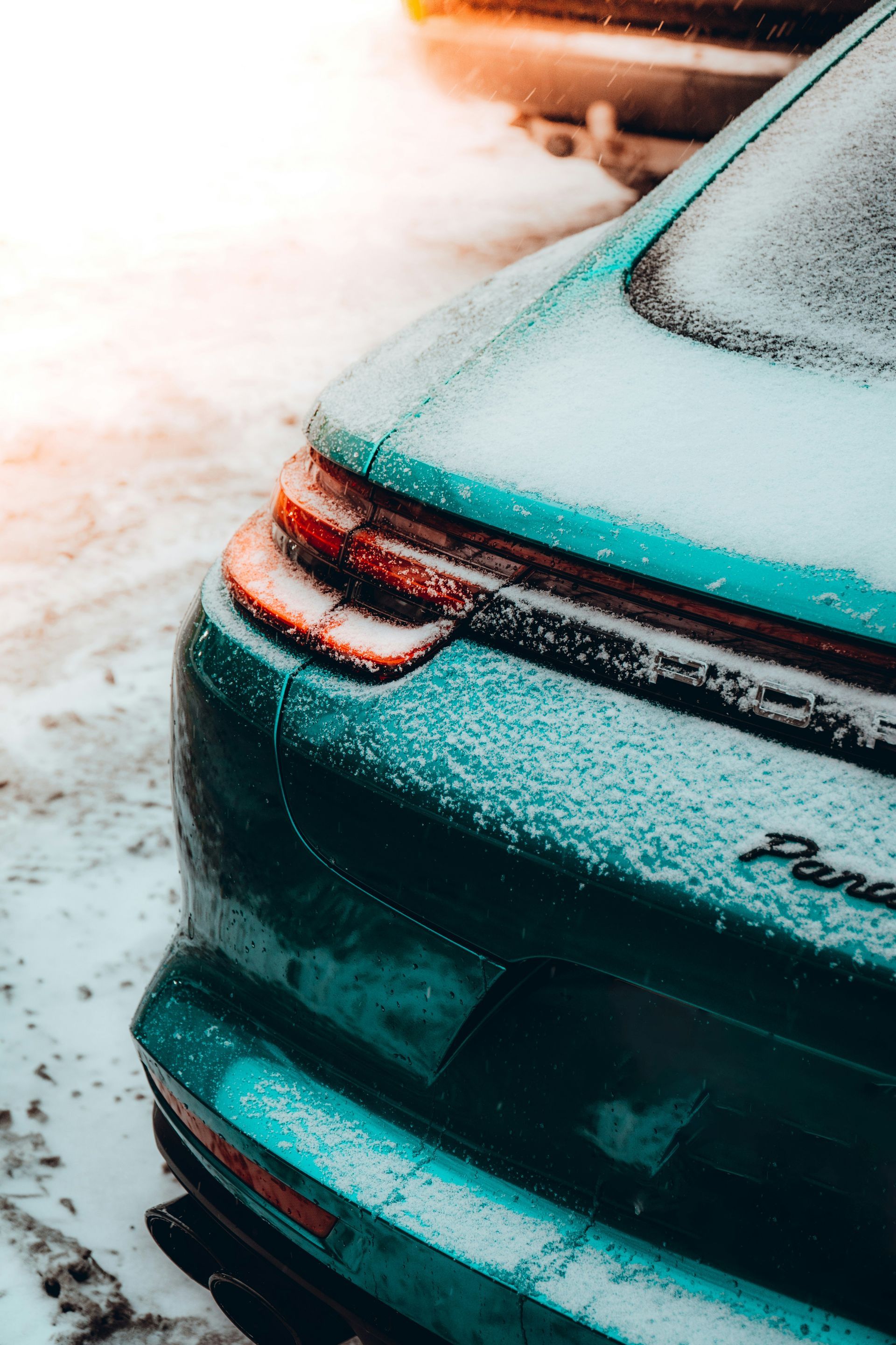Rear of a teal car dusted with snow, showing the taillight and trunk in a snowy lot
