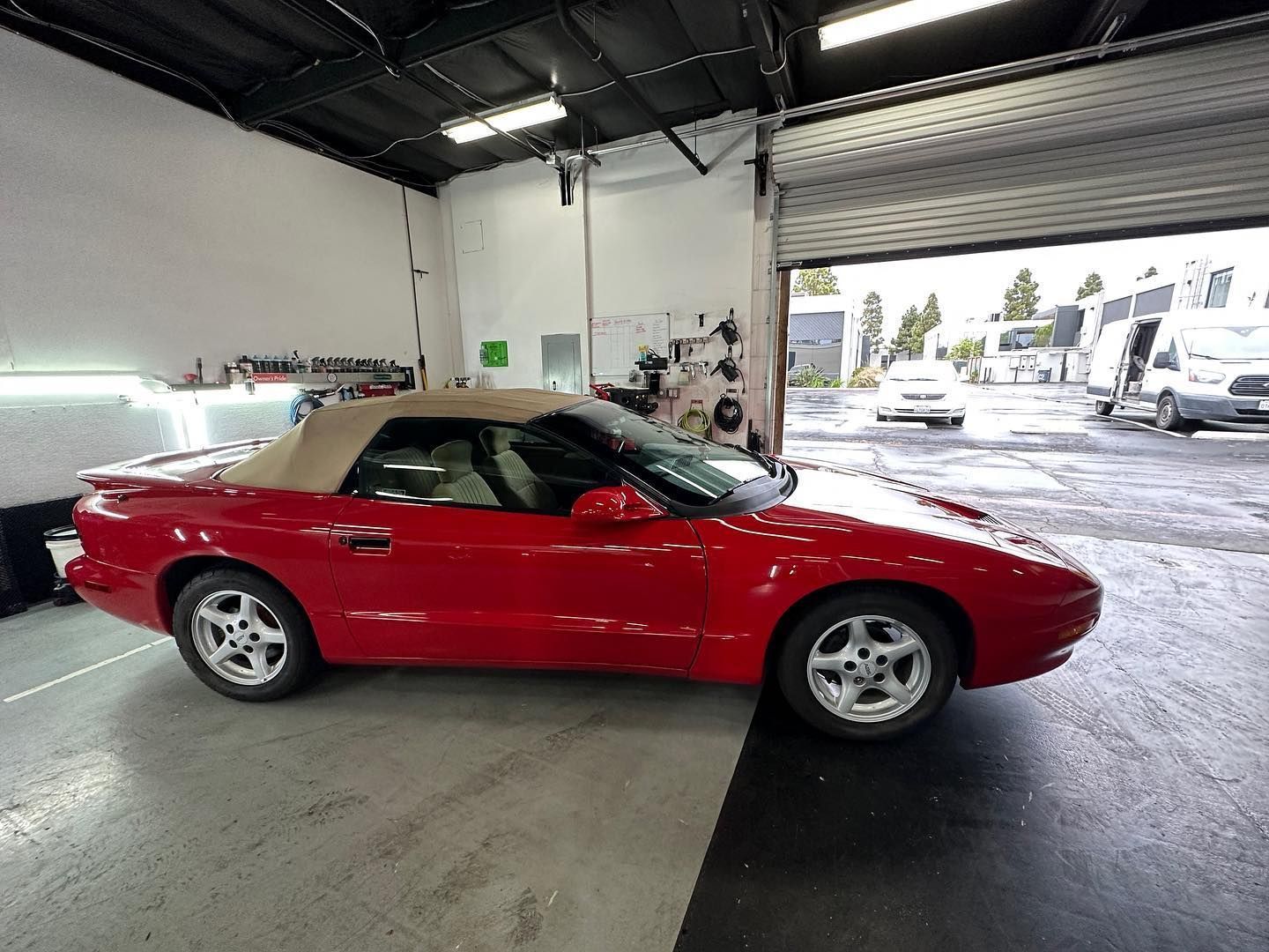 Red convertible sports car in a garage with its roof up, viewed from the side.