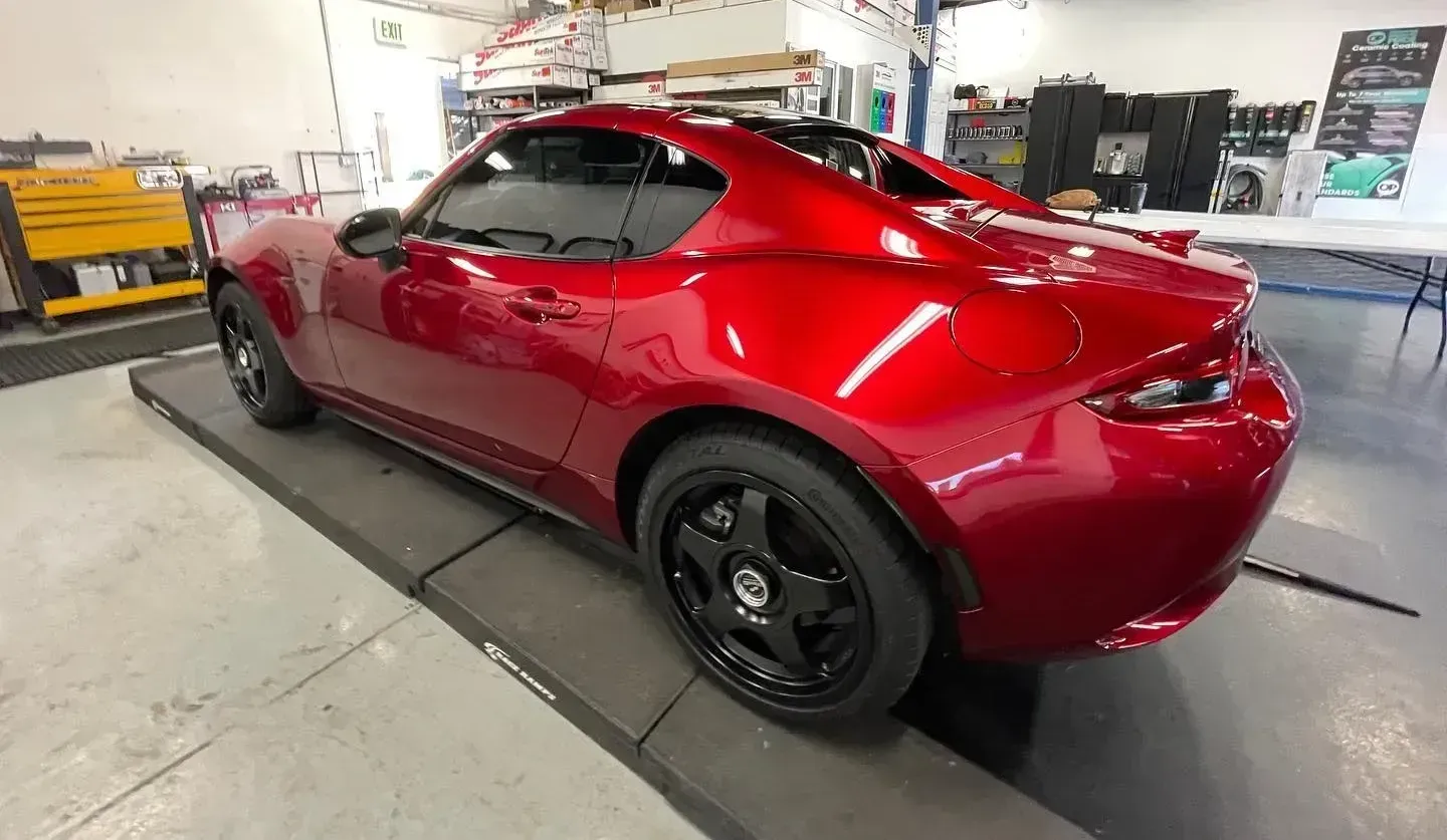 Red sports coupe in a garage on a lift, side view, glossy paint and black wheels