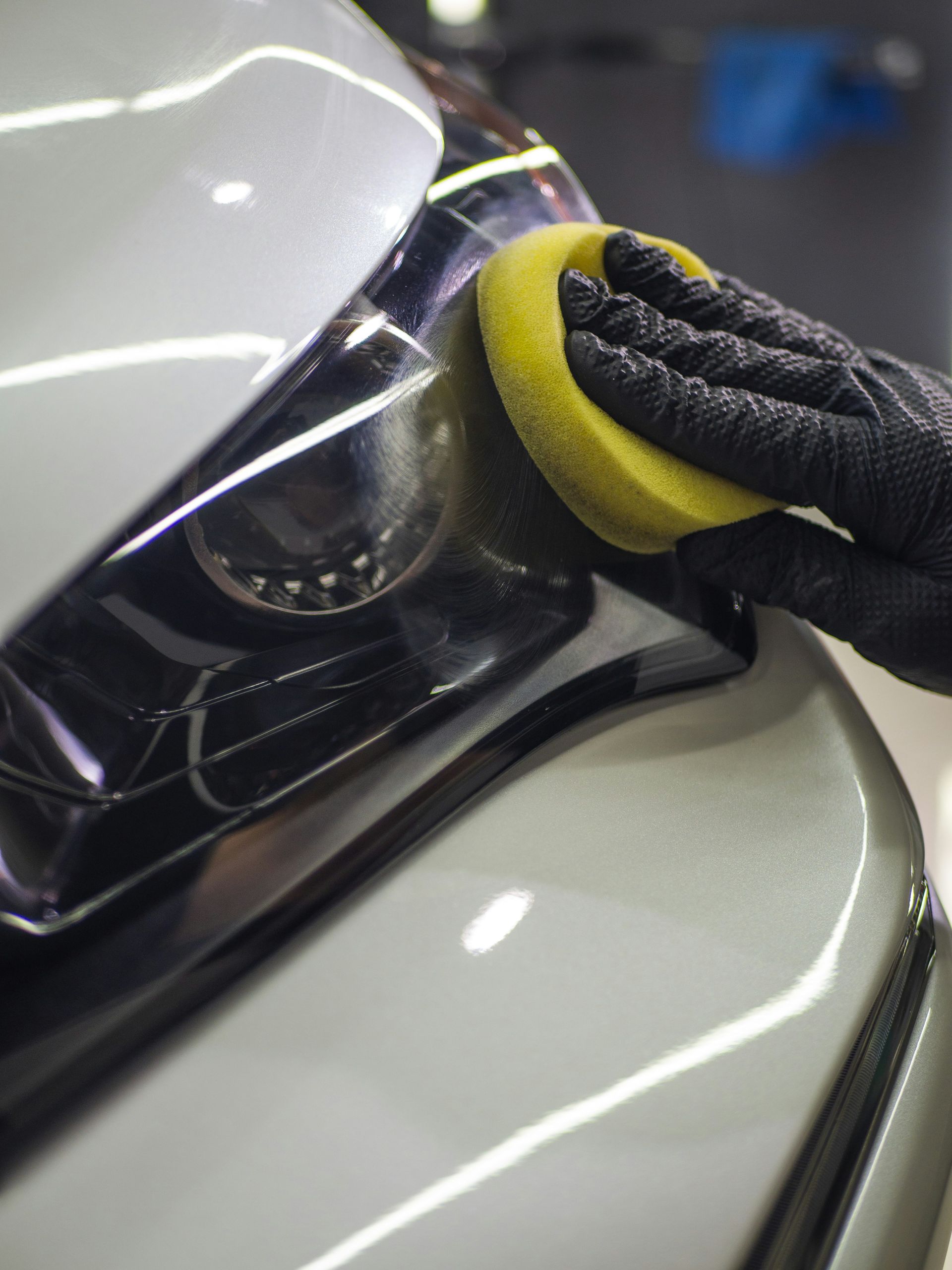 Gloved hand polishing a car headlight with a yellow sponge, close-up.
