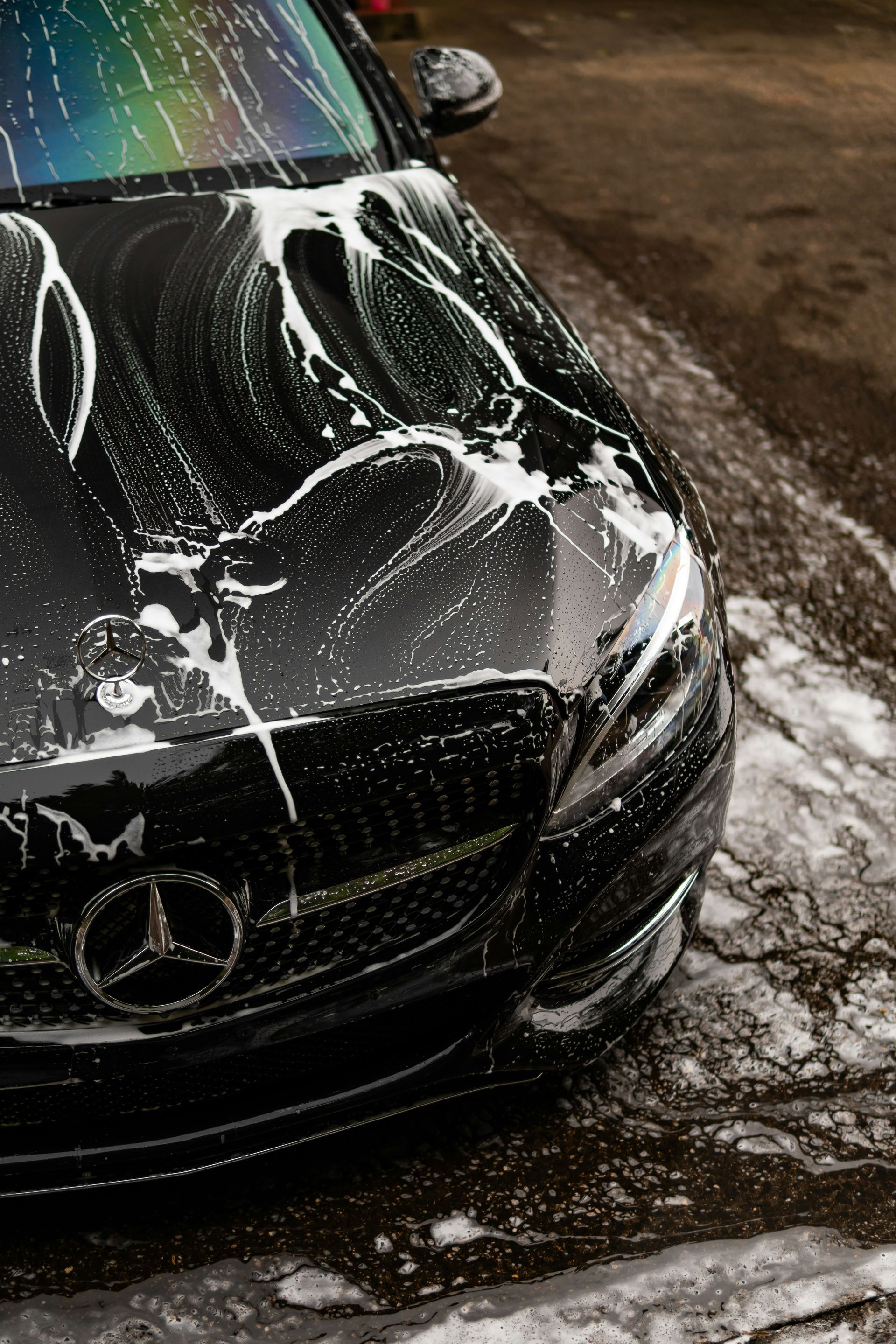 Black Mercedes being washed with soap and water on a wet driveway